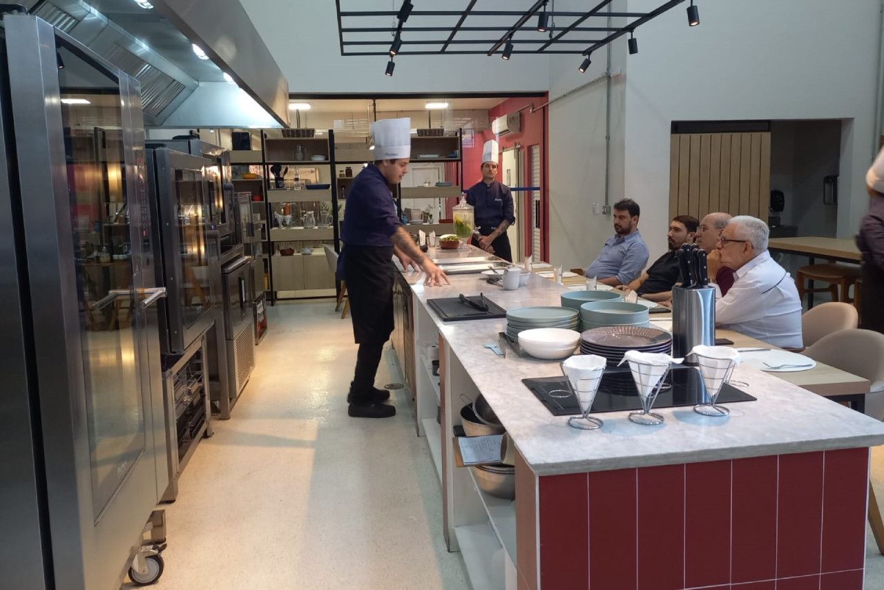 Um grupo de pessoas está sentado em mesas em uma cozinha enquanto um chef prepara comida.
