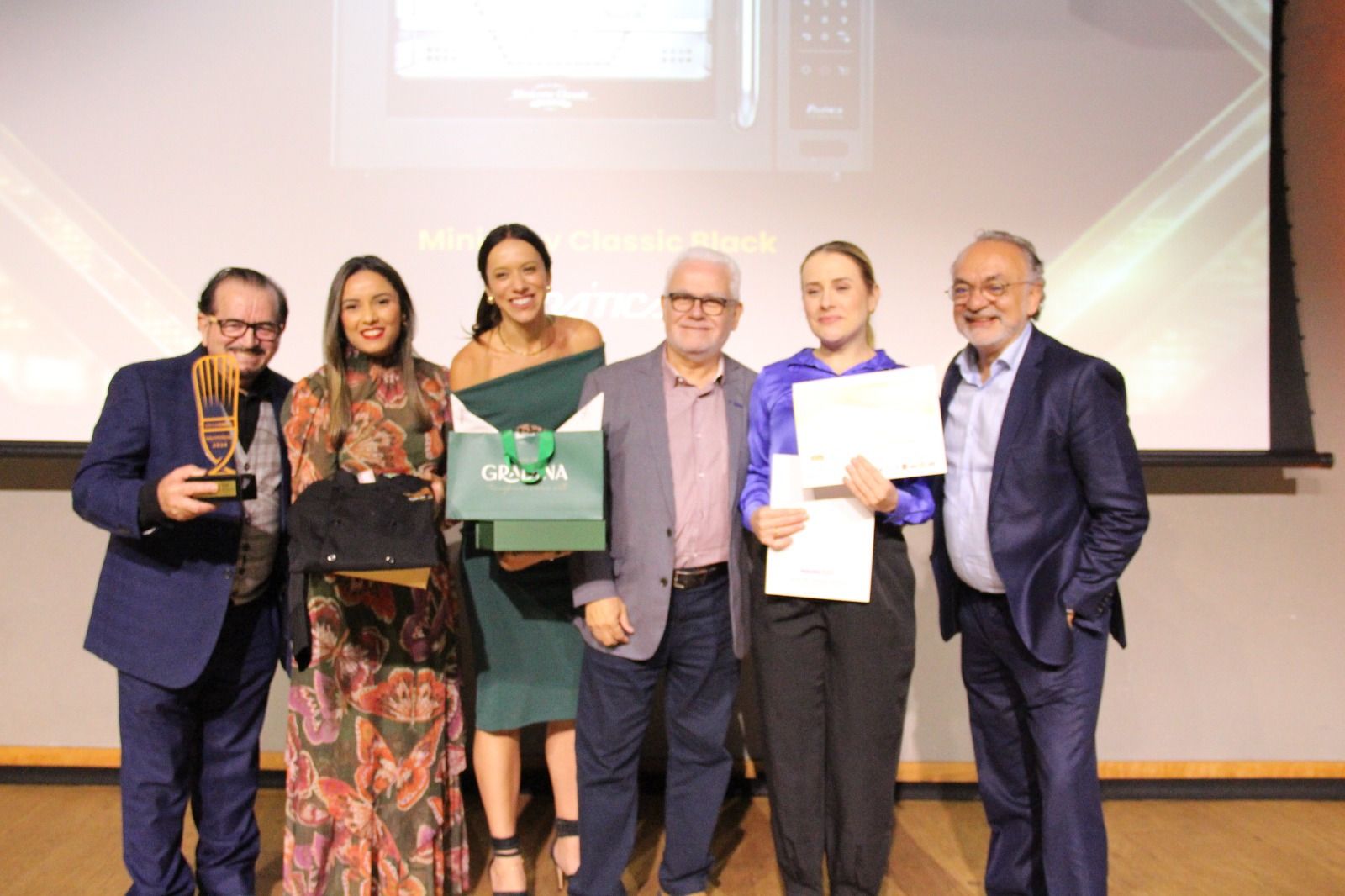 Um grupo de pessoas em pé, uma ao lado da outra, em um palco, segurando prêmios.