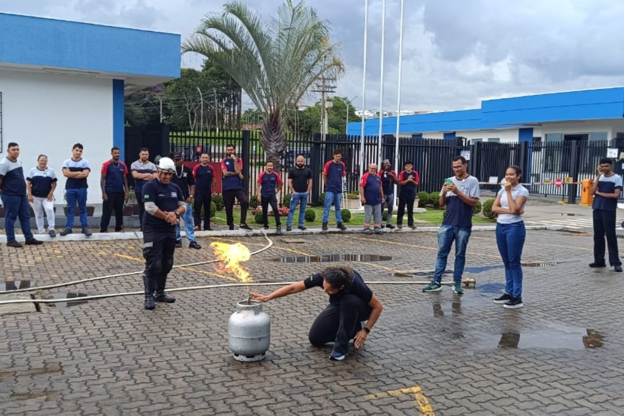 Treinamento de segurança contra incêndio: Uma pessoa demonstra como acender um fogo a gás enquanto outras observam, em um ambiente externo.