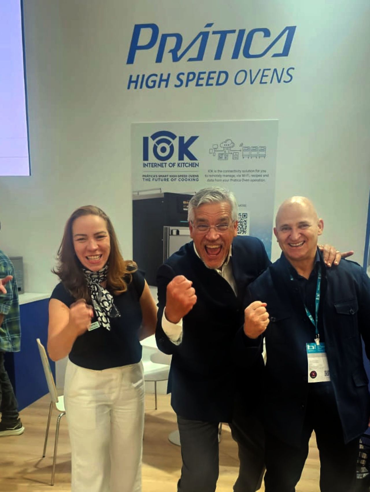 Três pessoas comemoram em frente a uma placa com a inscrição 