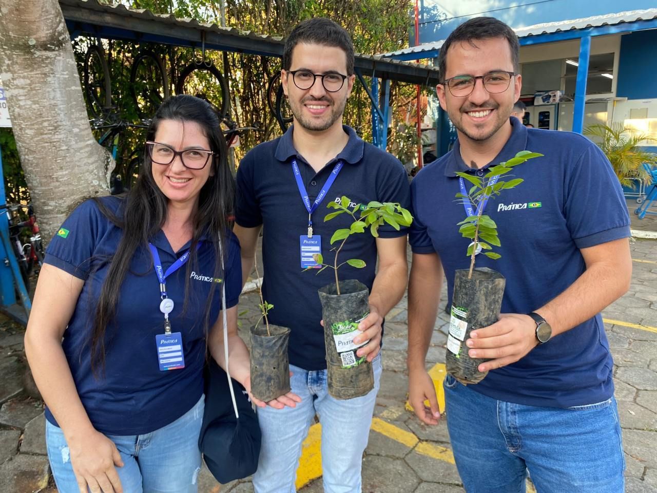 Três pessoas estão de pé, uma ao lado da outra, segurando vasos de plantas.
