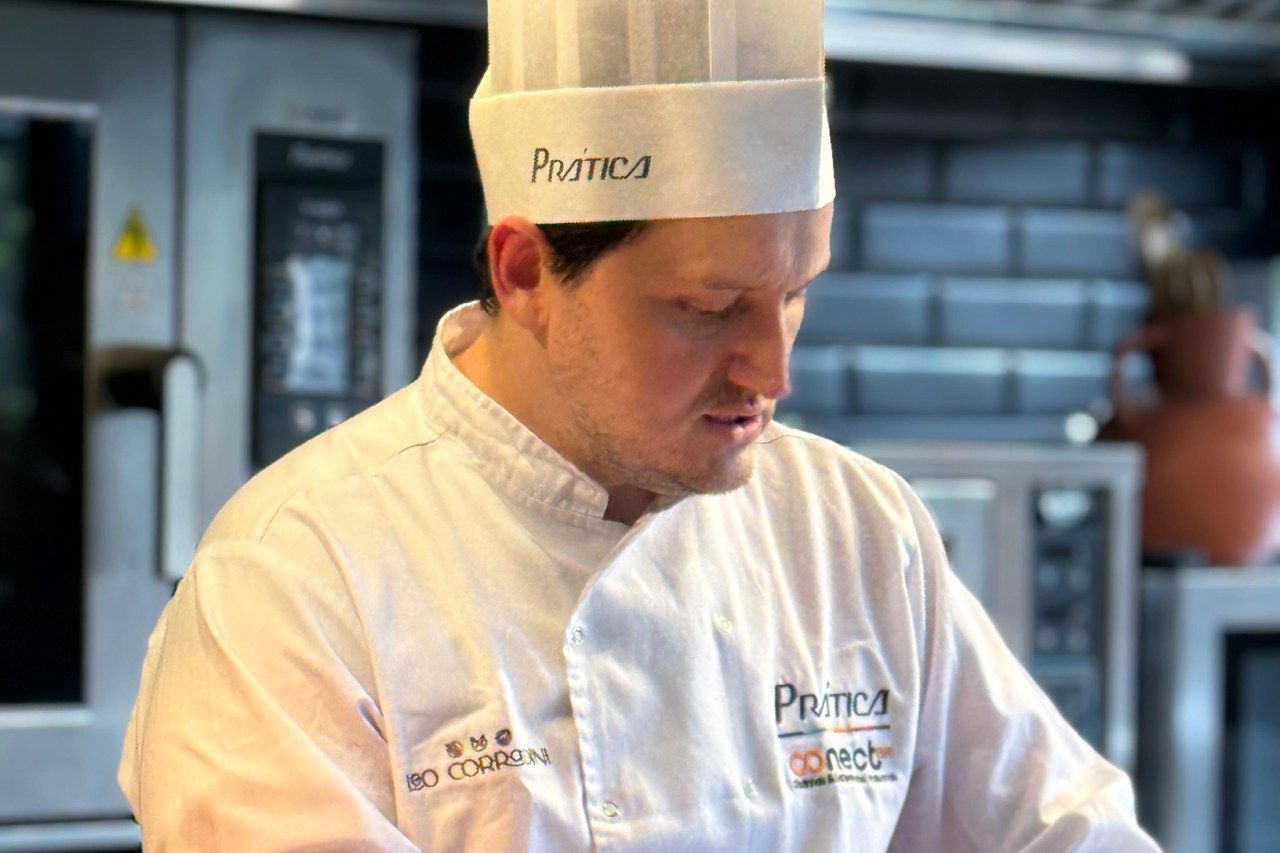 Chef de uniforme branco e chapéu, focado em um ambiente de cozinha.
