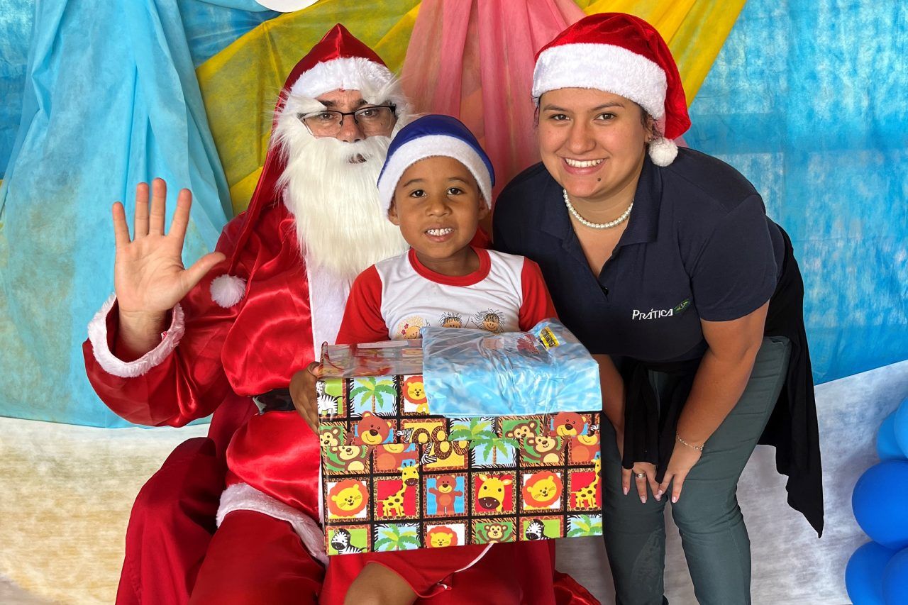Um garotinho está sentado ao lado do Papai Noel e segurando uma caixa de presente.