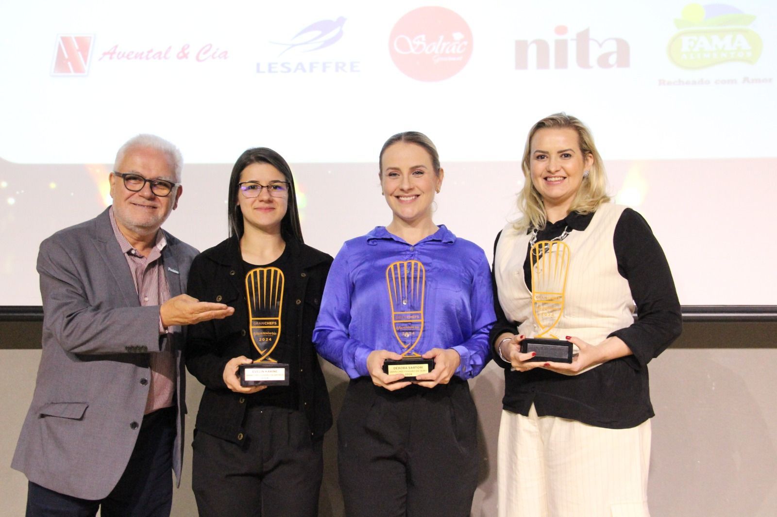Um grupo de pessoas de pé, uma ao lado da outra, segurando troféus.