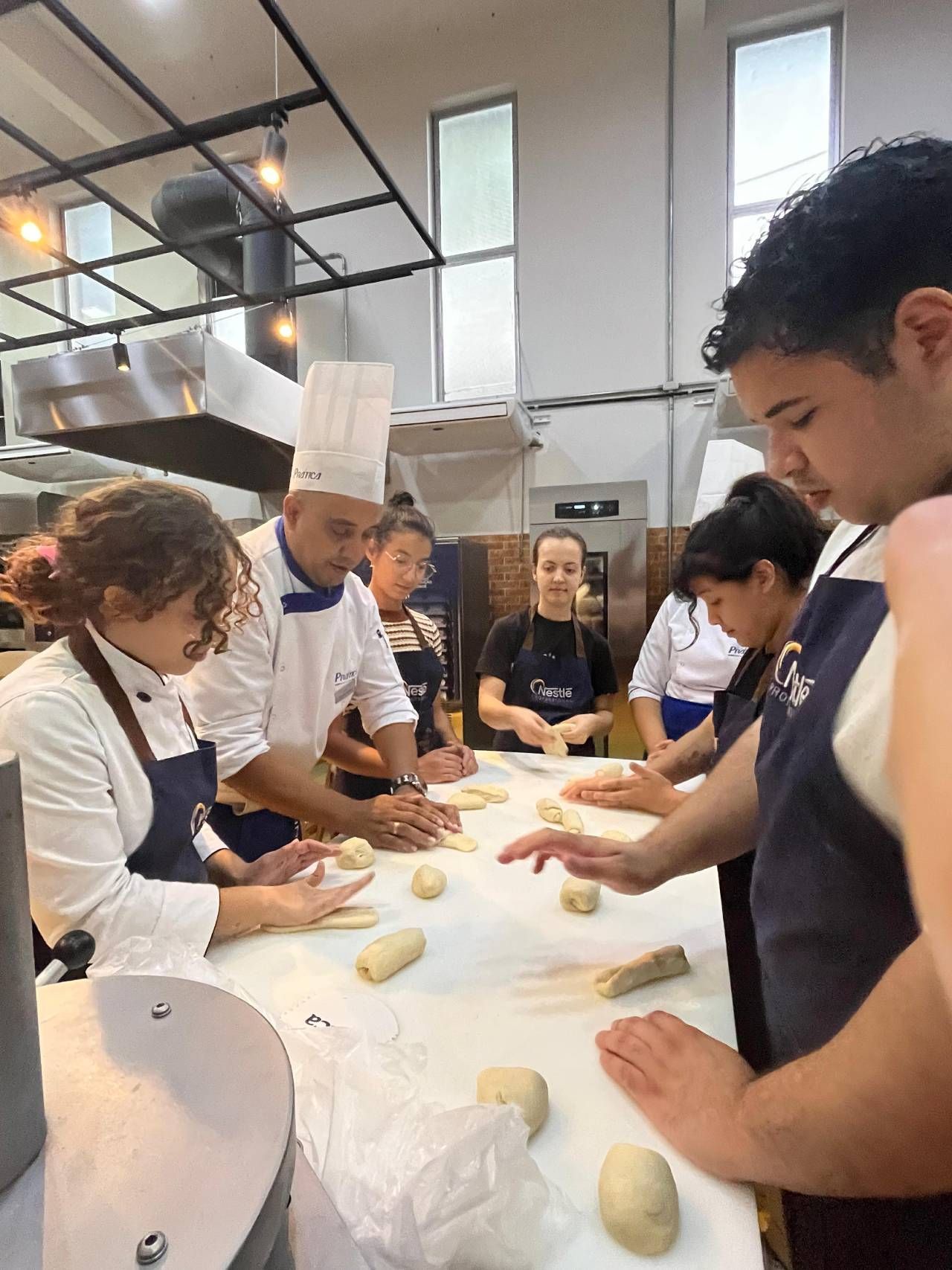 Um grupo de pessoas está em pé ao redor de uma mesa na cozinha.