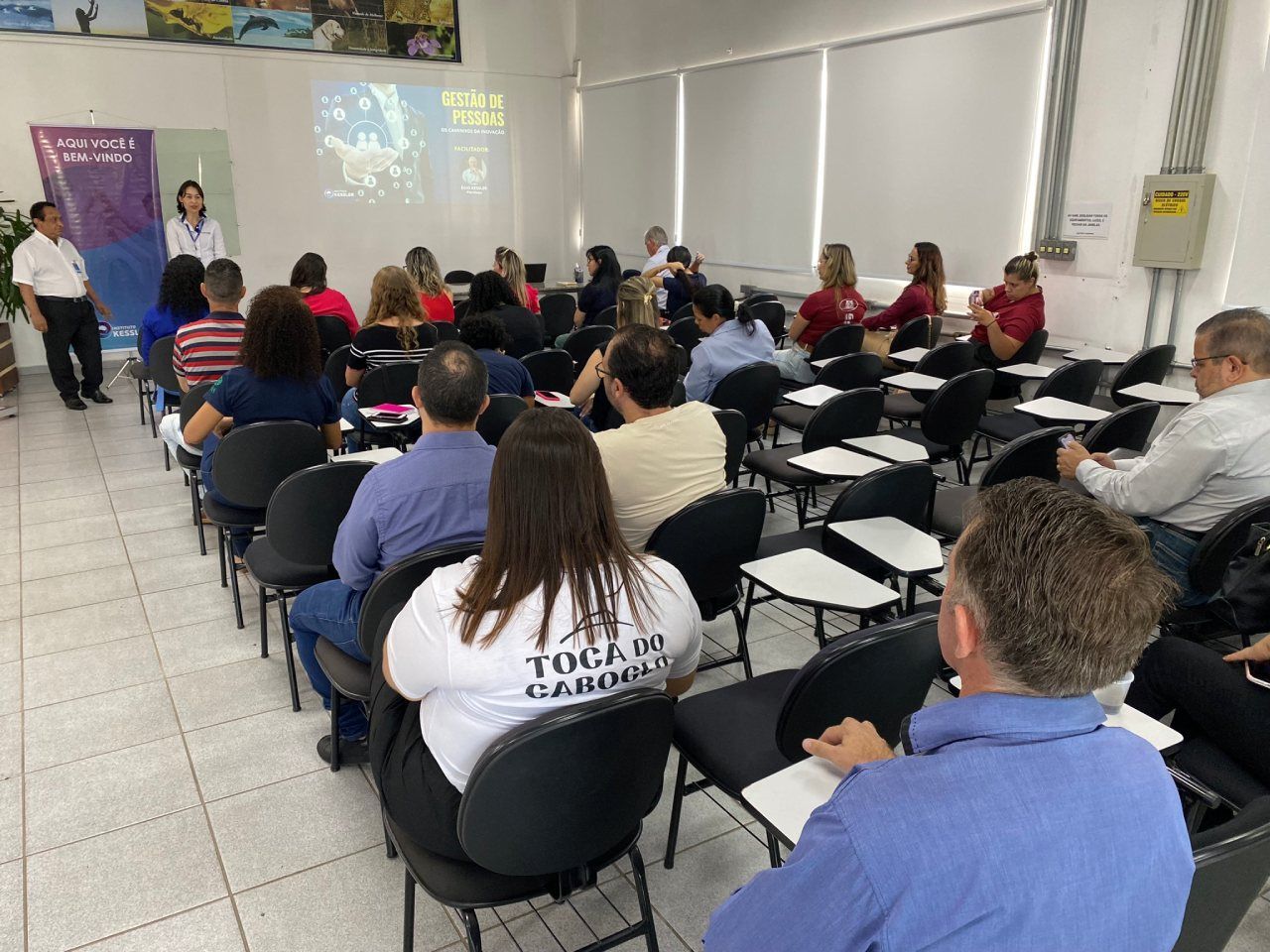 Um grupo de pessoas está sentado em uma sala de aula assistindo a uma apresentação.