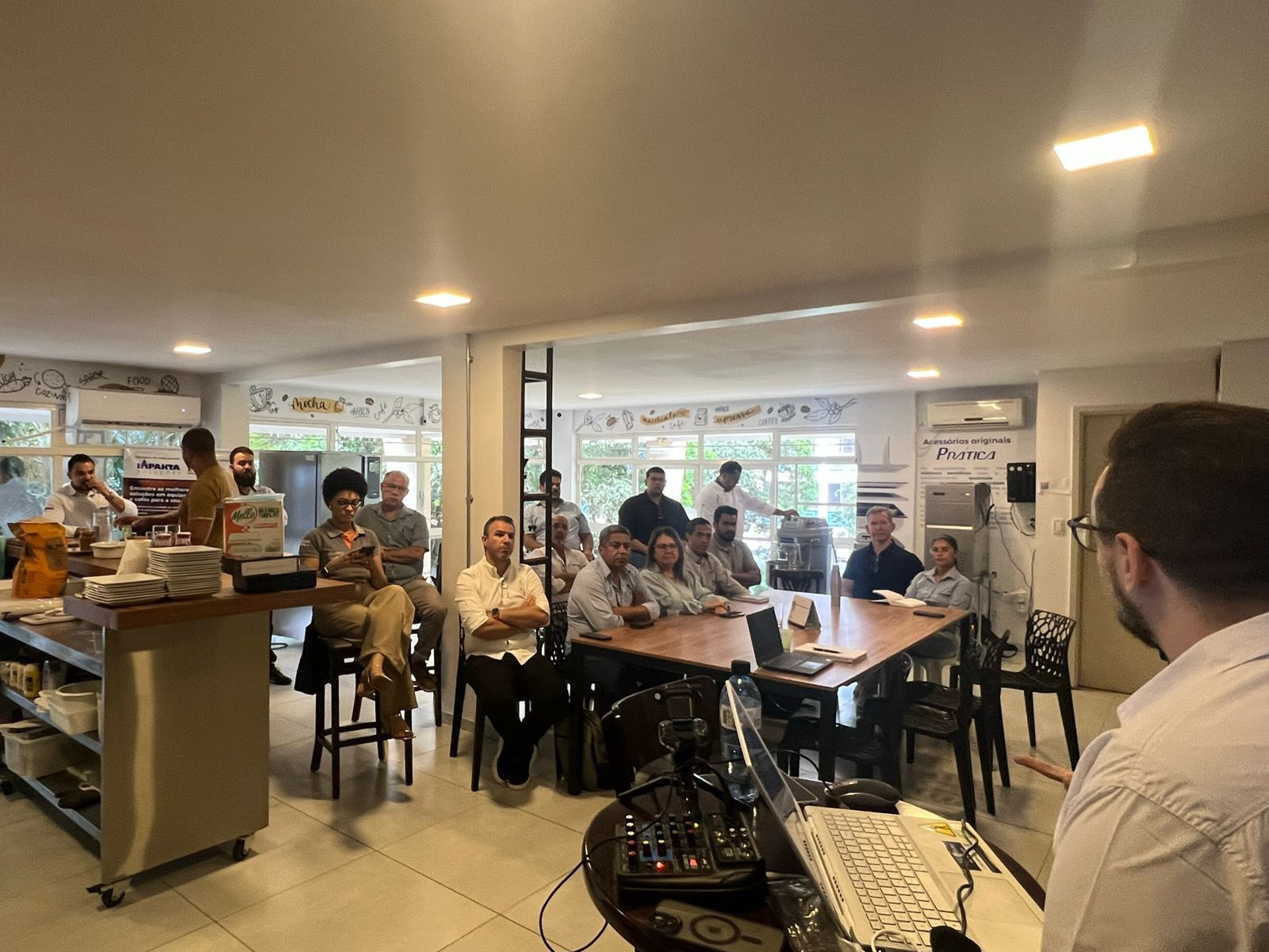 Um homem está fazendo uma apresentação para um grupo de pessoas sentadas em mesas em uma sala.