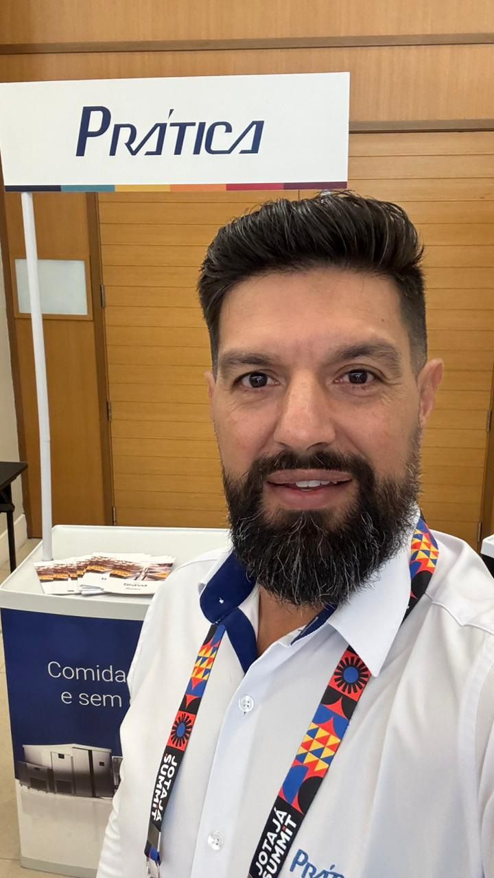 Um homem com barba está parado em frente a uma placa que diz pratica.