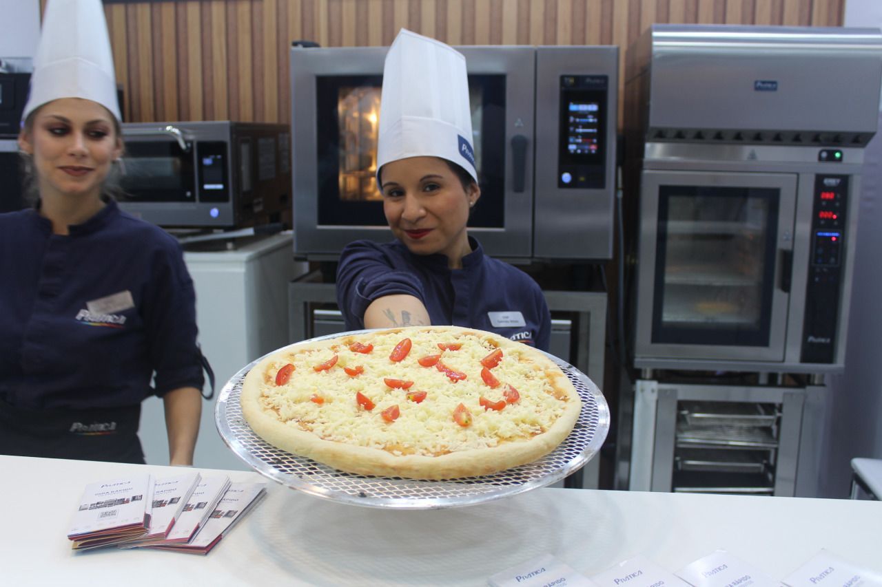 Uma mulher com chapéu de chef está segurando uma pizza