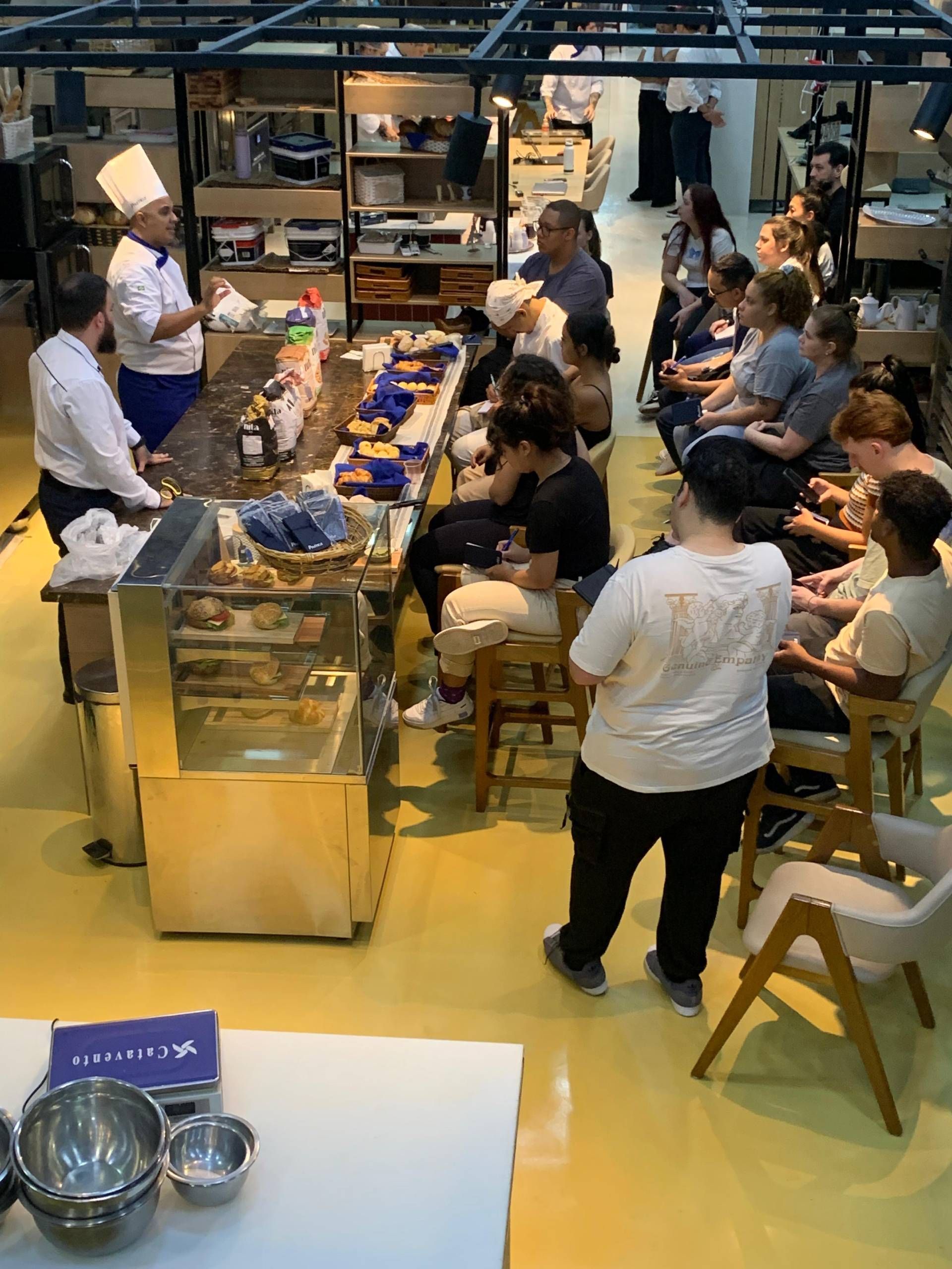 Um grupo de pessoas está sentado em uma longa mesa na cozinha.