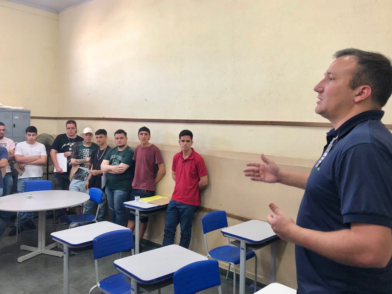 Um homem está parado na frente de um grupo de pessoas em uma sala de aula.