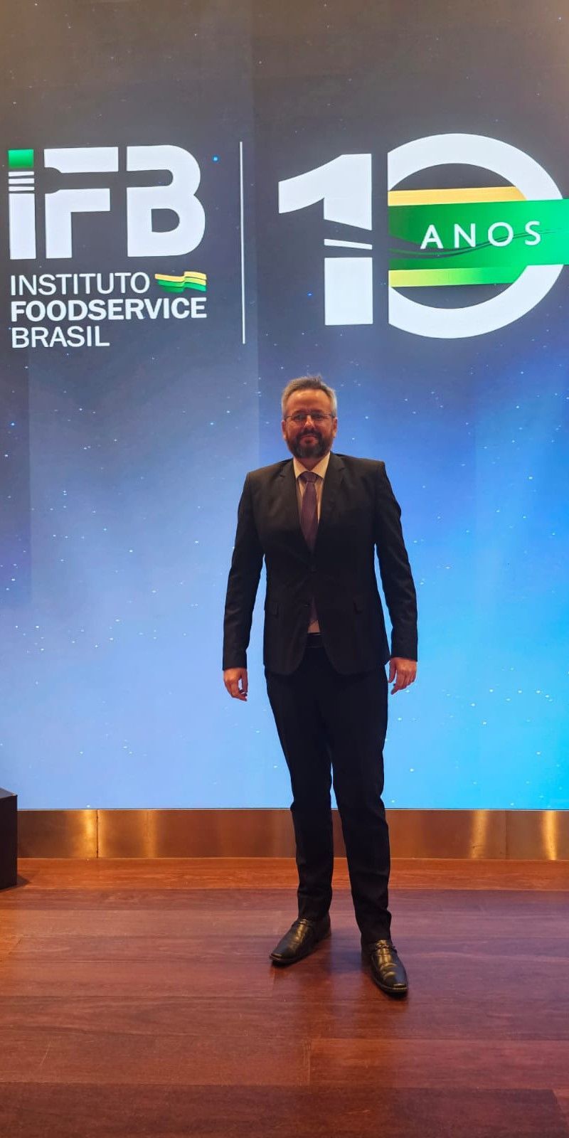 Um homem de terno e gravata está parado em frente a uma tela grande.