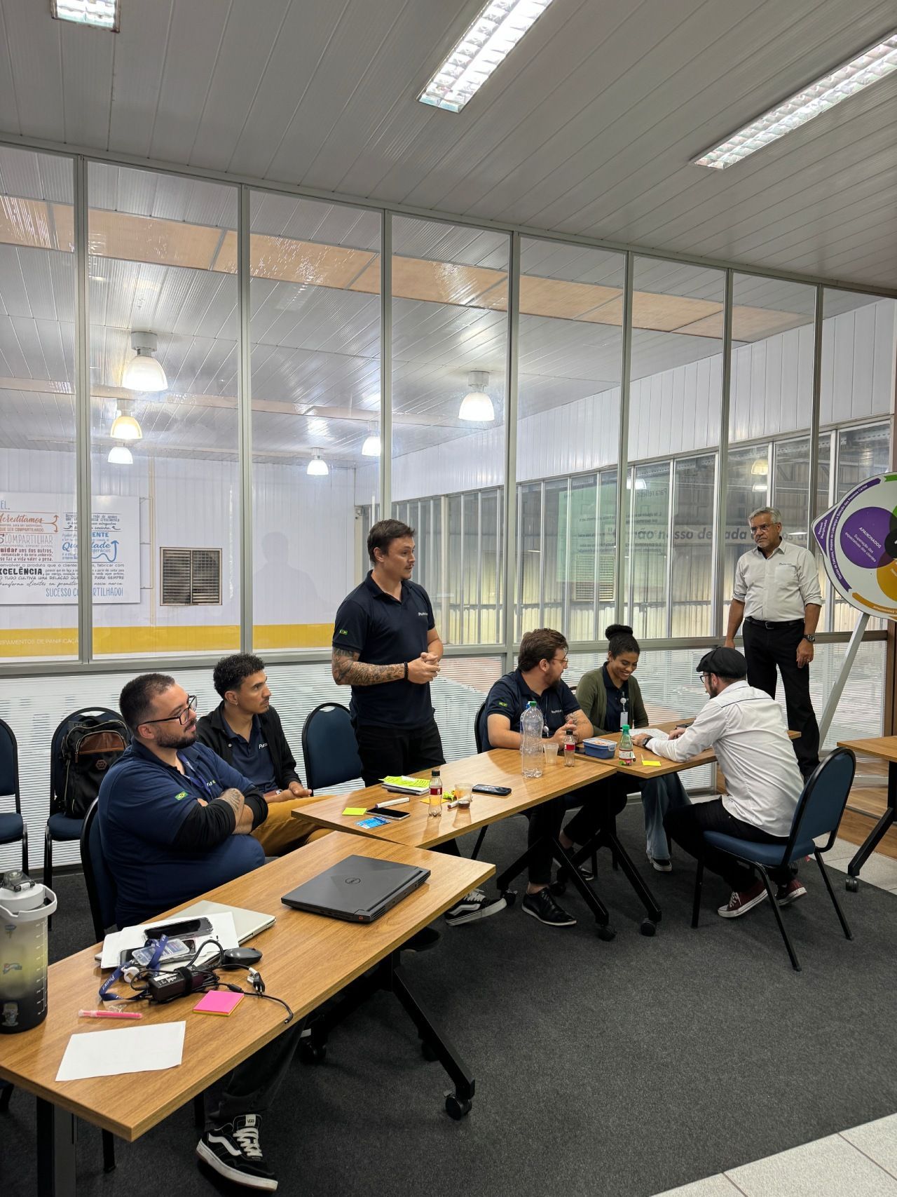 Um grupo de pessoas senta-se e fica em pé ao redor de mesas