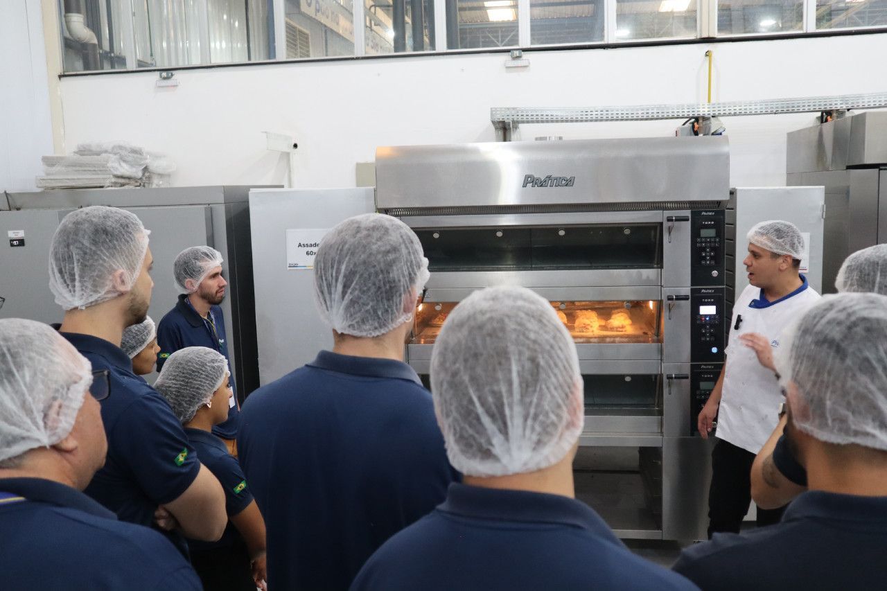 Um grupo de pessoas está em pé ao redor de um forno em uma cozinha.