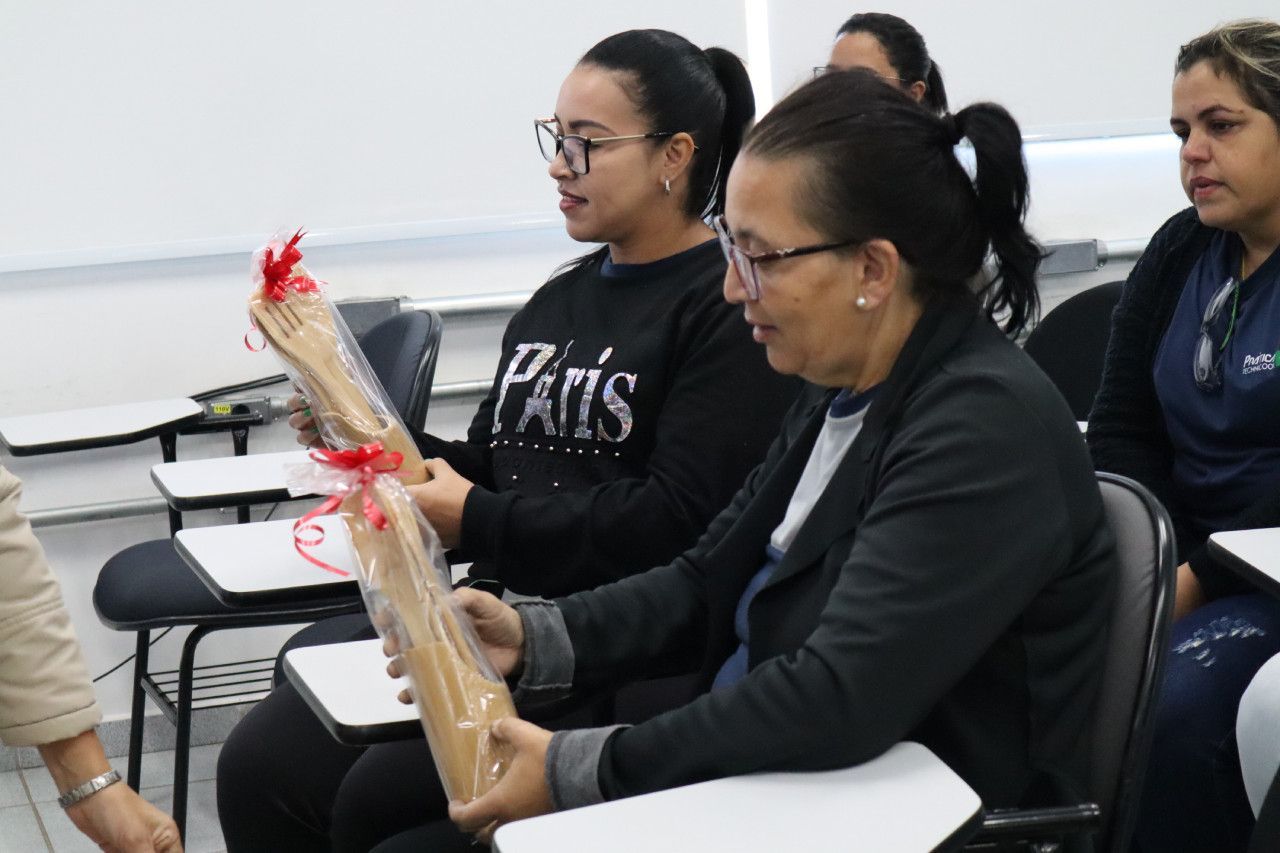 Um grupo de mulheres está sentada em uma sala de aula segurando presentes.