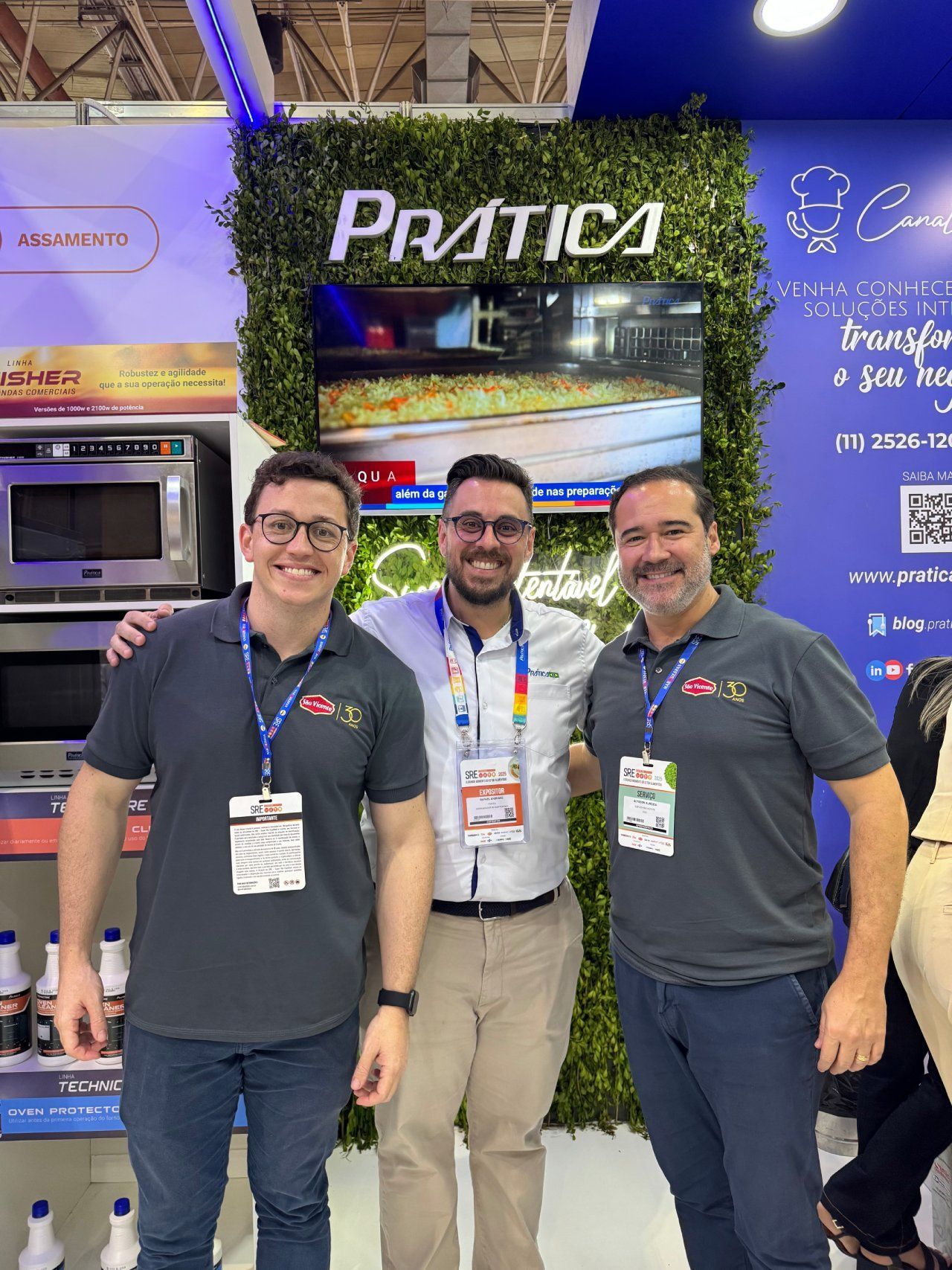 Três homens estão posando para uma foto em frente a um forno de micro-ondas.