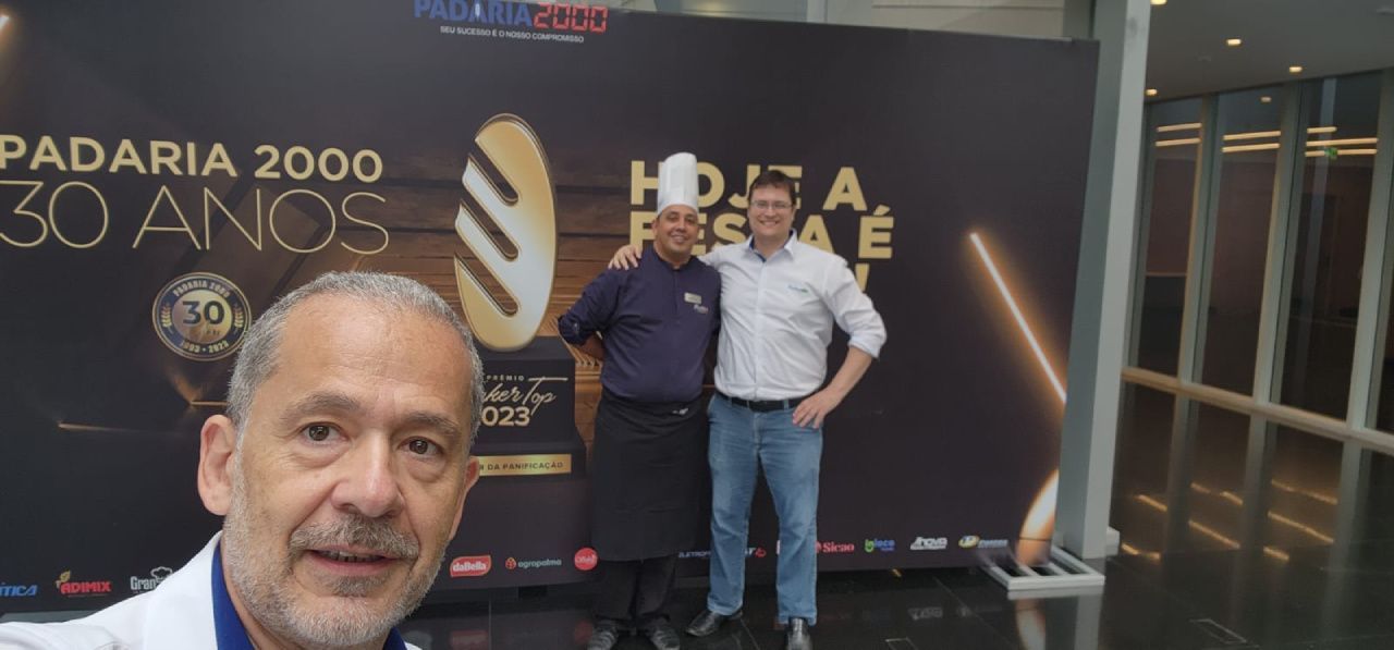 Dois homens estão posando para uma foto em frente a uma placa que diz padaria 2000 30 anos.