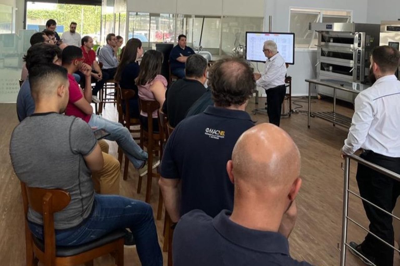 Um grupo de pessoas está sentado em cadeiras ouvindo uma apresentação