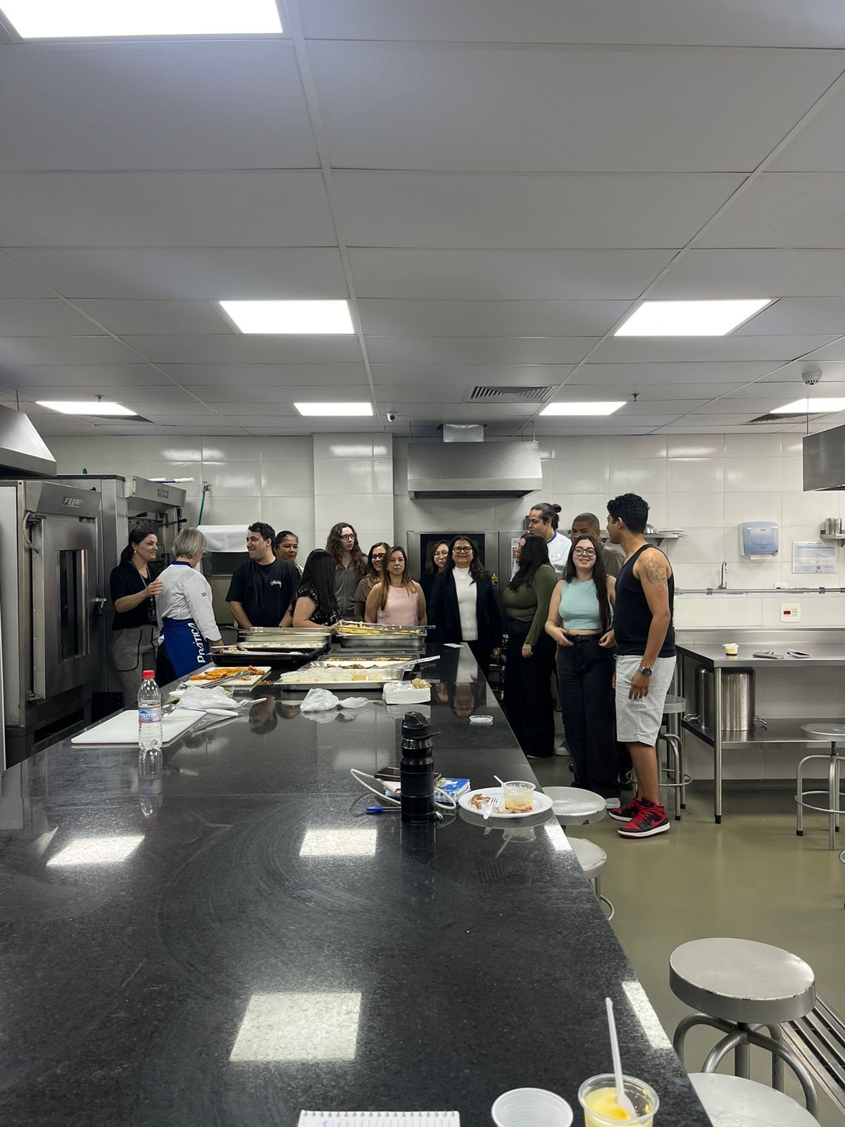 Um grupo de pessoas está em pé ao redor de um balcão na cozinha.