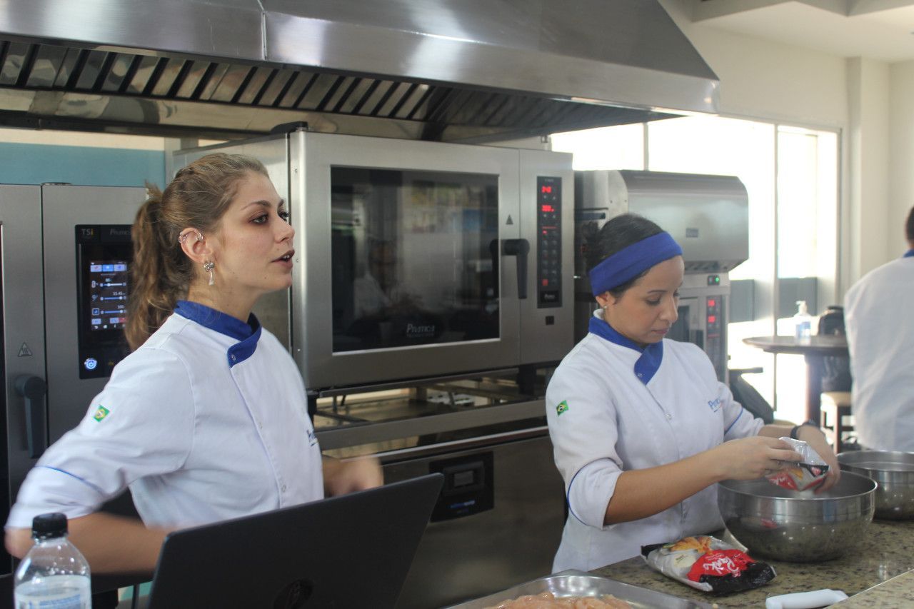 Duas mulheres estão trabalhando em uma cozinha e uma está usando um laptop