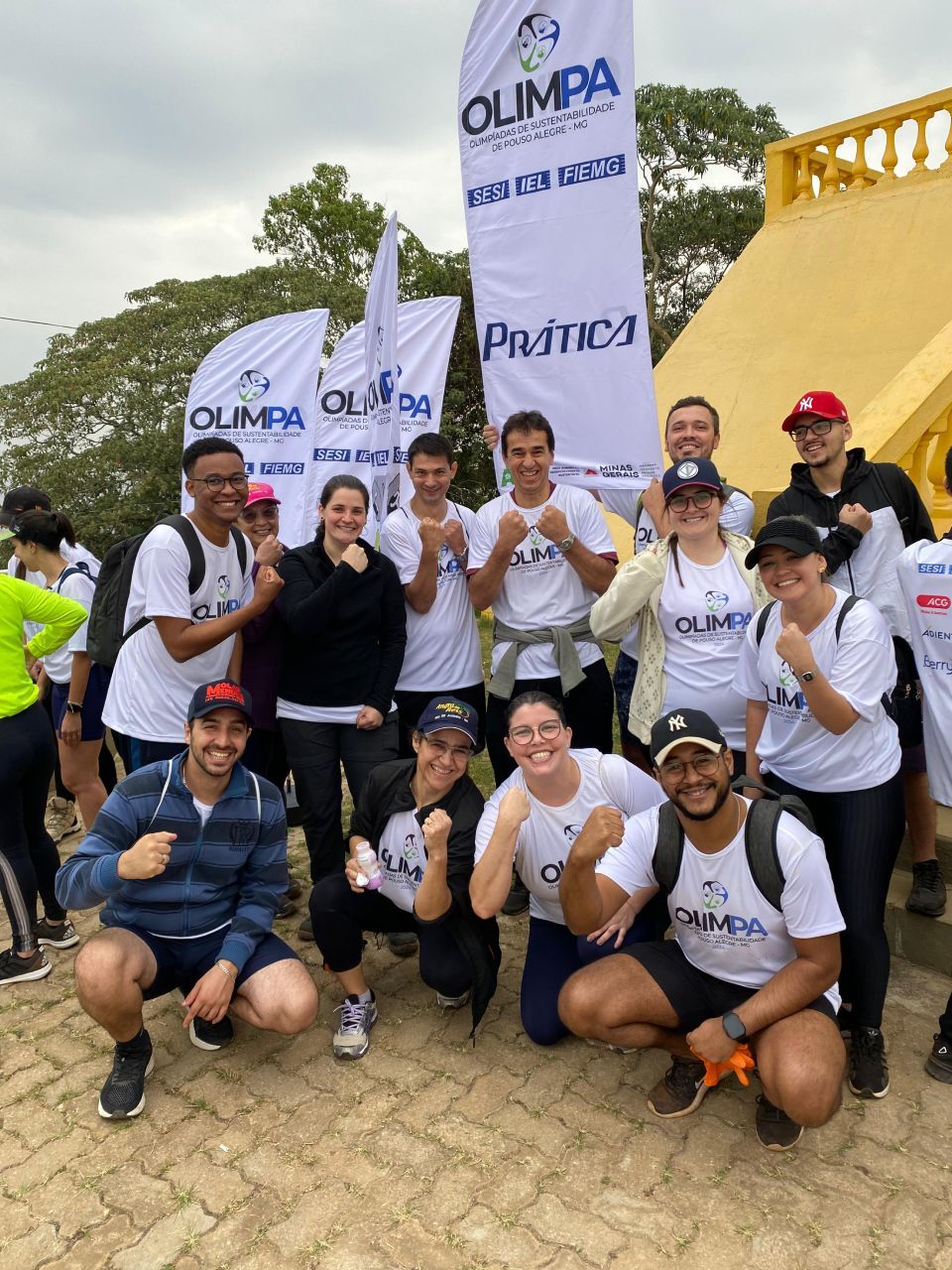 Um grupo de pessoas posando para uma foto com bandeiras de Olímpia ao fundo.
