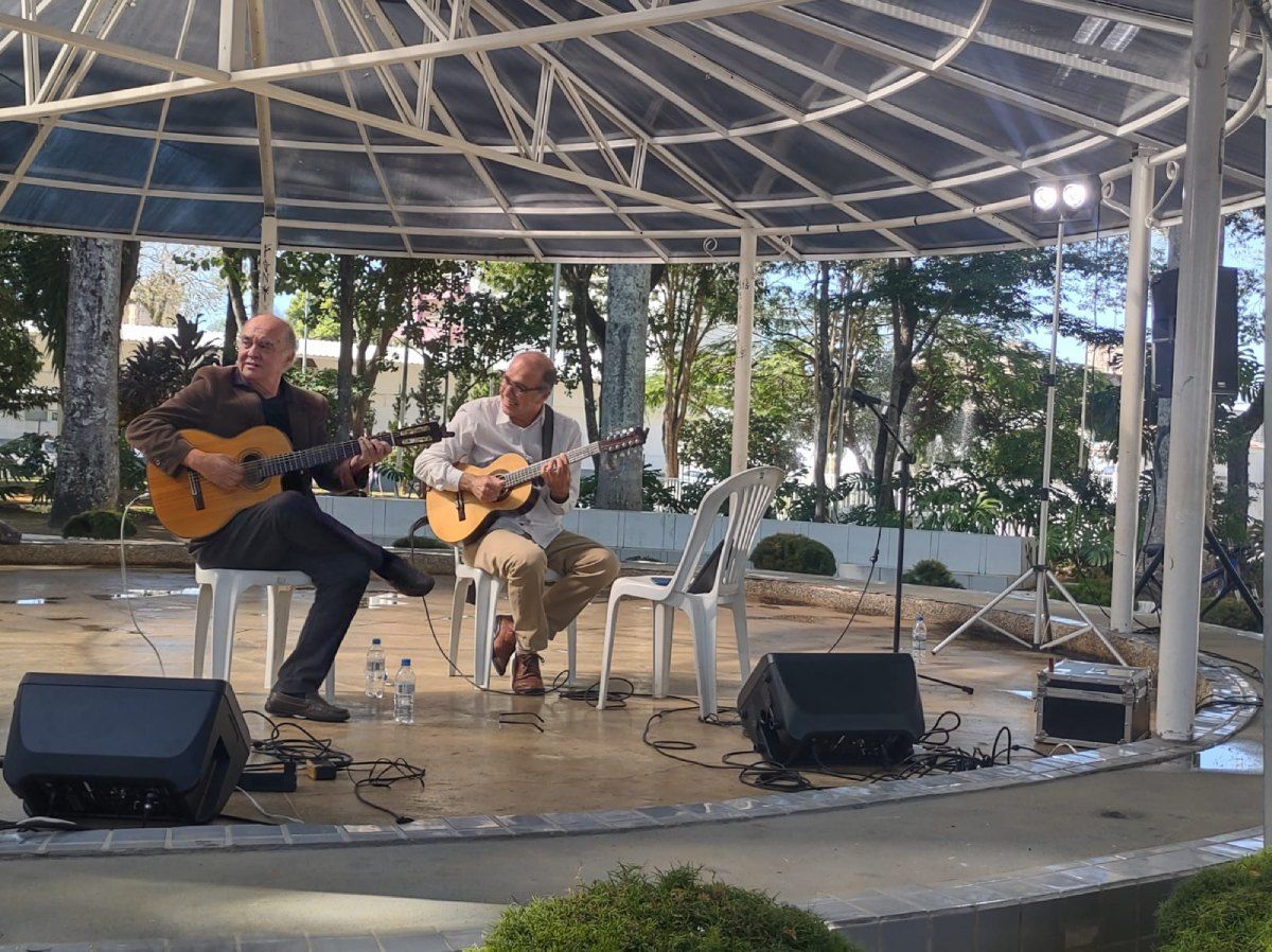 Dois homens estão tocando violão em um palco sob um dossel.