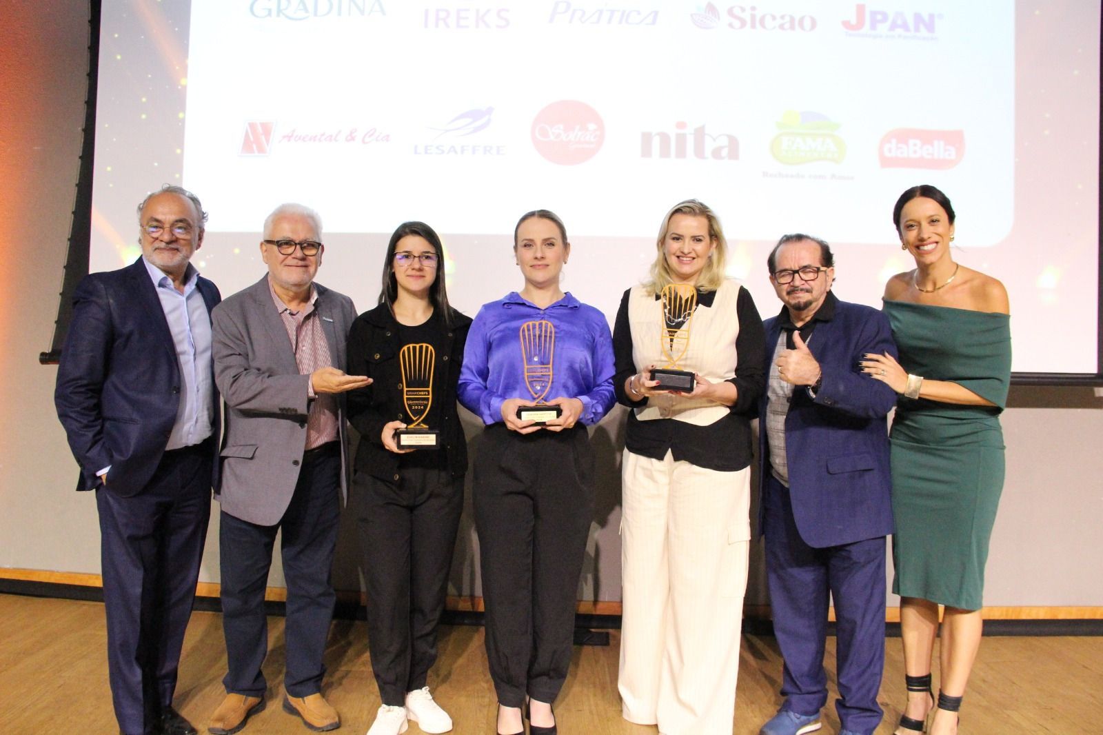 Um grupo de pessoas de pé, uma ao lado da outra, segurando troféus.