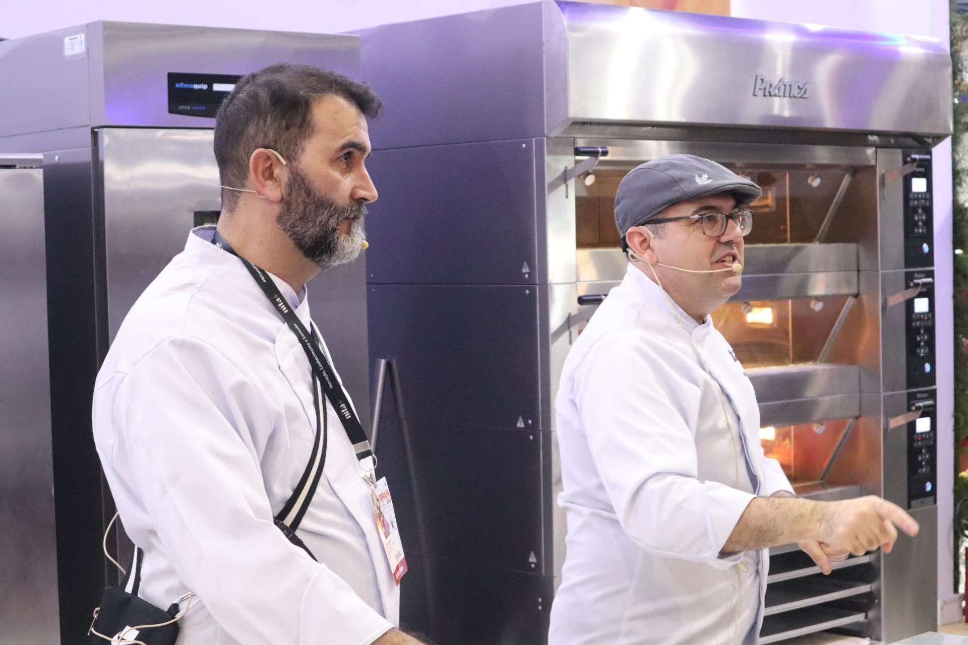 Dois homens estão de pé, um ao lado do outro, em frente a um forno.