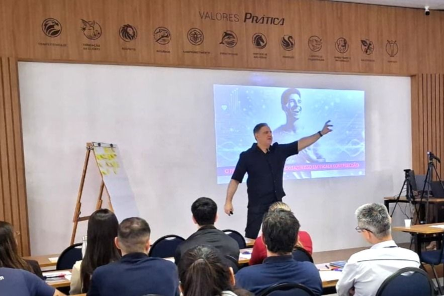 Um homem faz uma apresentação para uma plateia. Ele aponta para uma tela com uma foto.