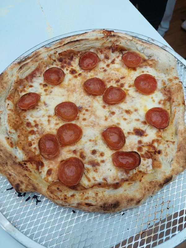Uma pizza de calabresa está sobre uma bandeja de metal em cima da mesa.