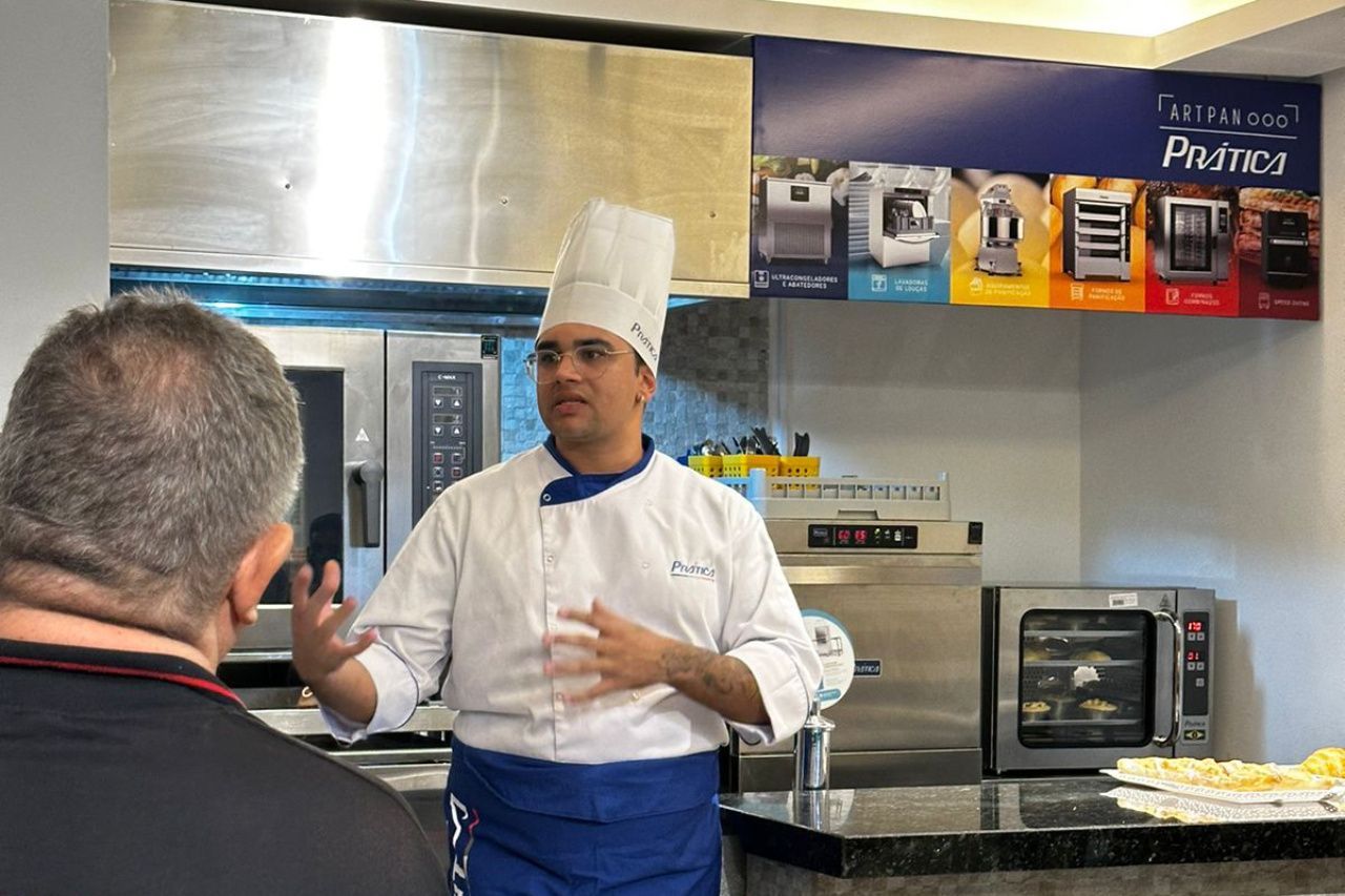 Um homem com chapéu de chef está conversando com outro homem na cozinha.