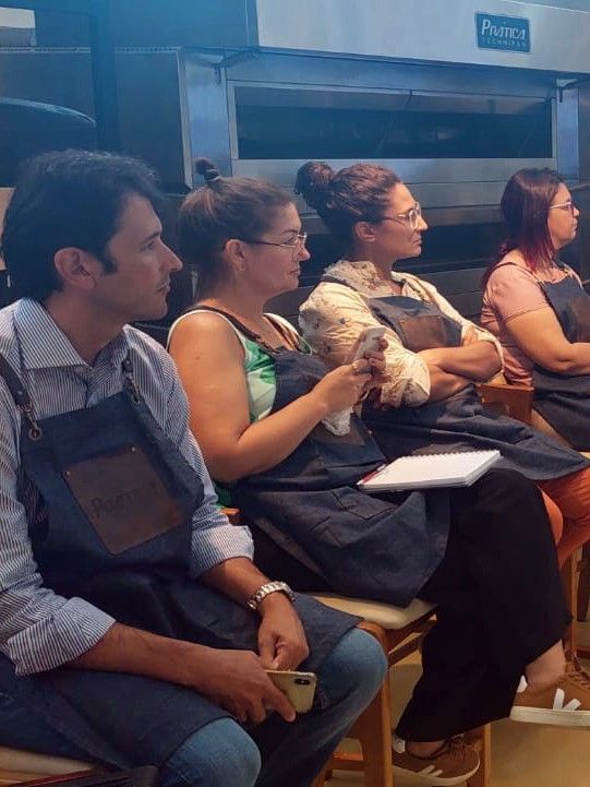 Um grupo de pessoas vestindo aventais está sentado em frente a um forno.