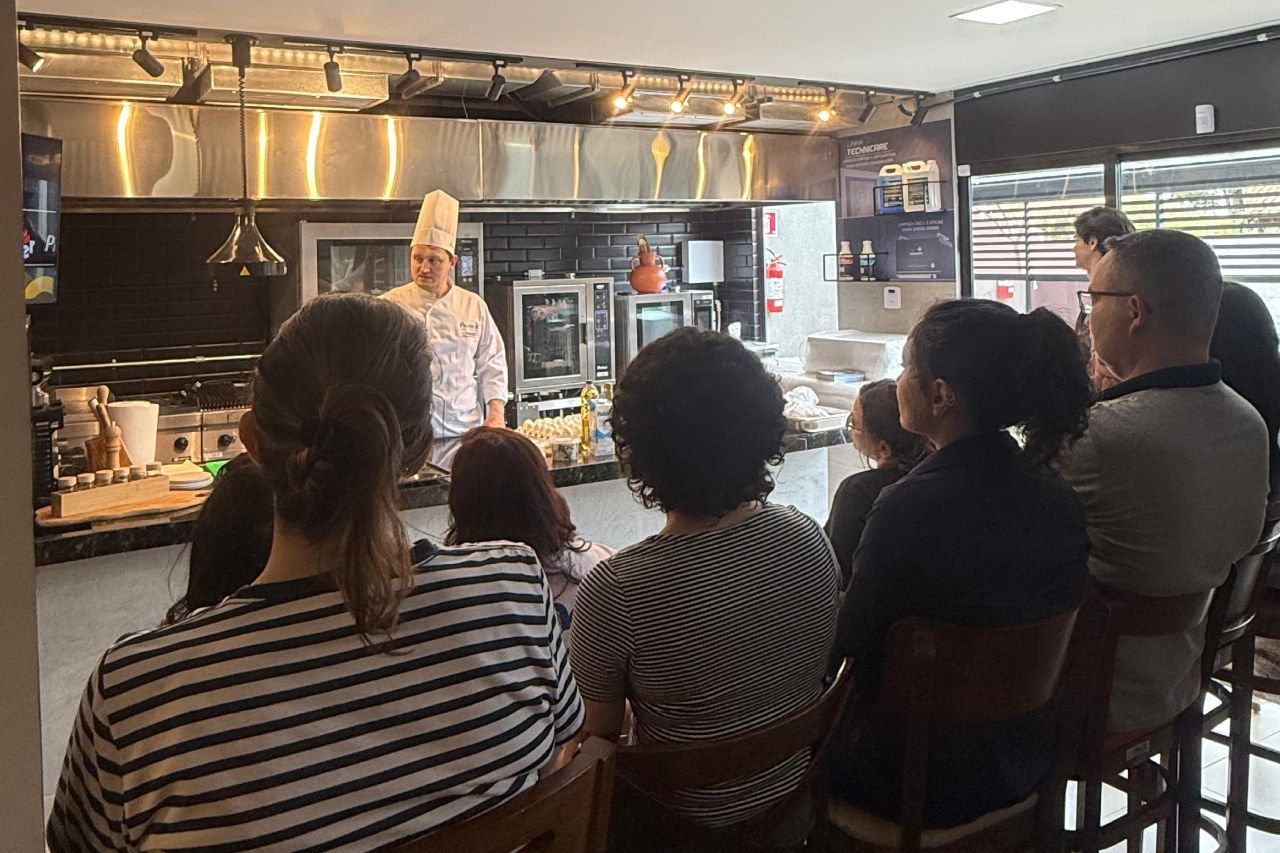 Chef demonstrando técnicas de culinária para um grupo em uma cozinha.