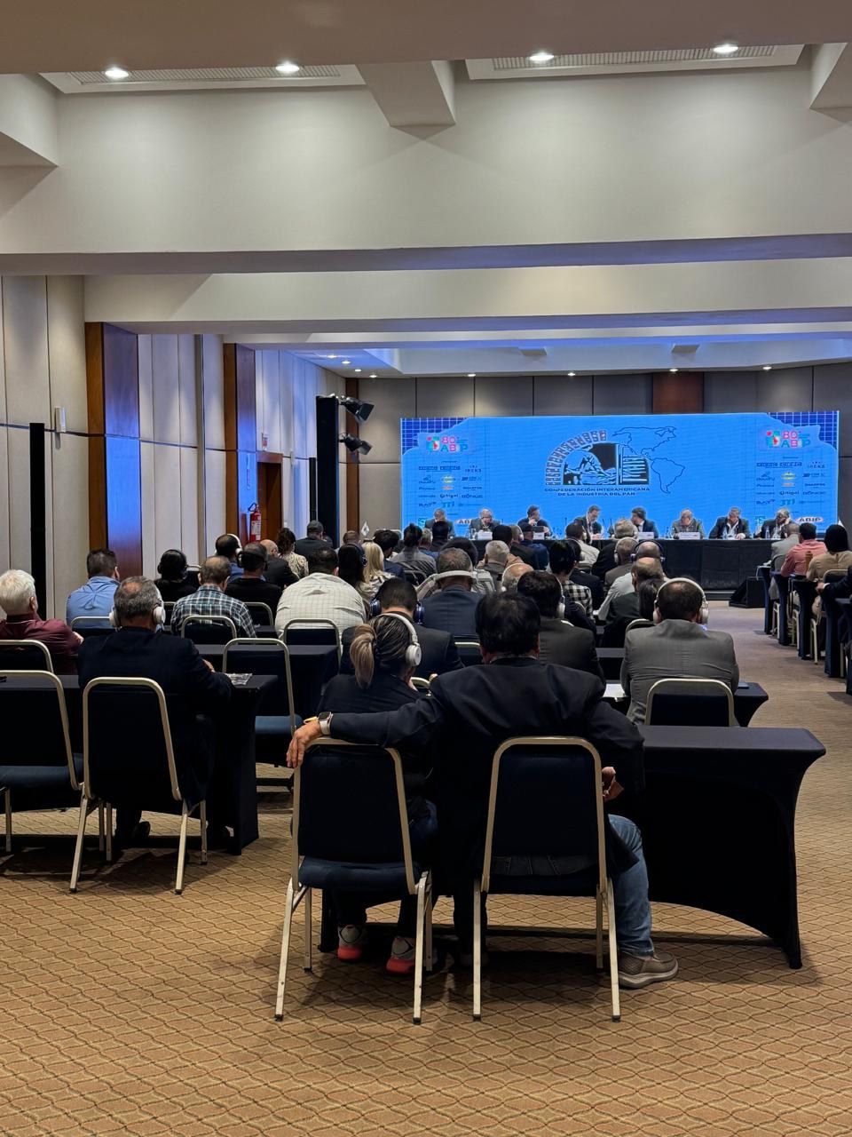 Uma grande sala cheia de pessoas sentadas em mesas e cadeiras.