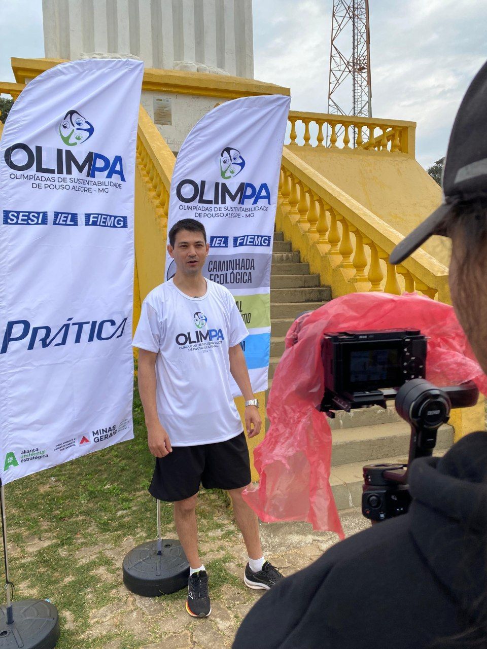 Um homem está parado na frente de uma câmera em frente a duas bandeiras de olympia