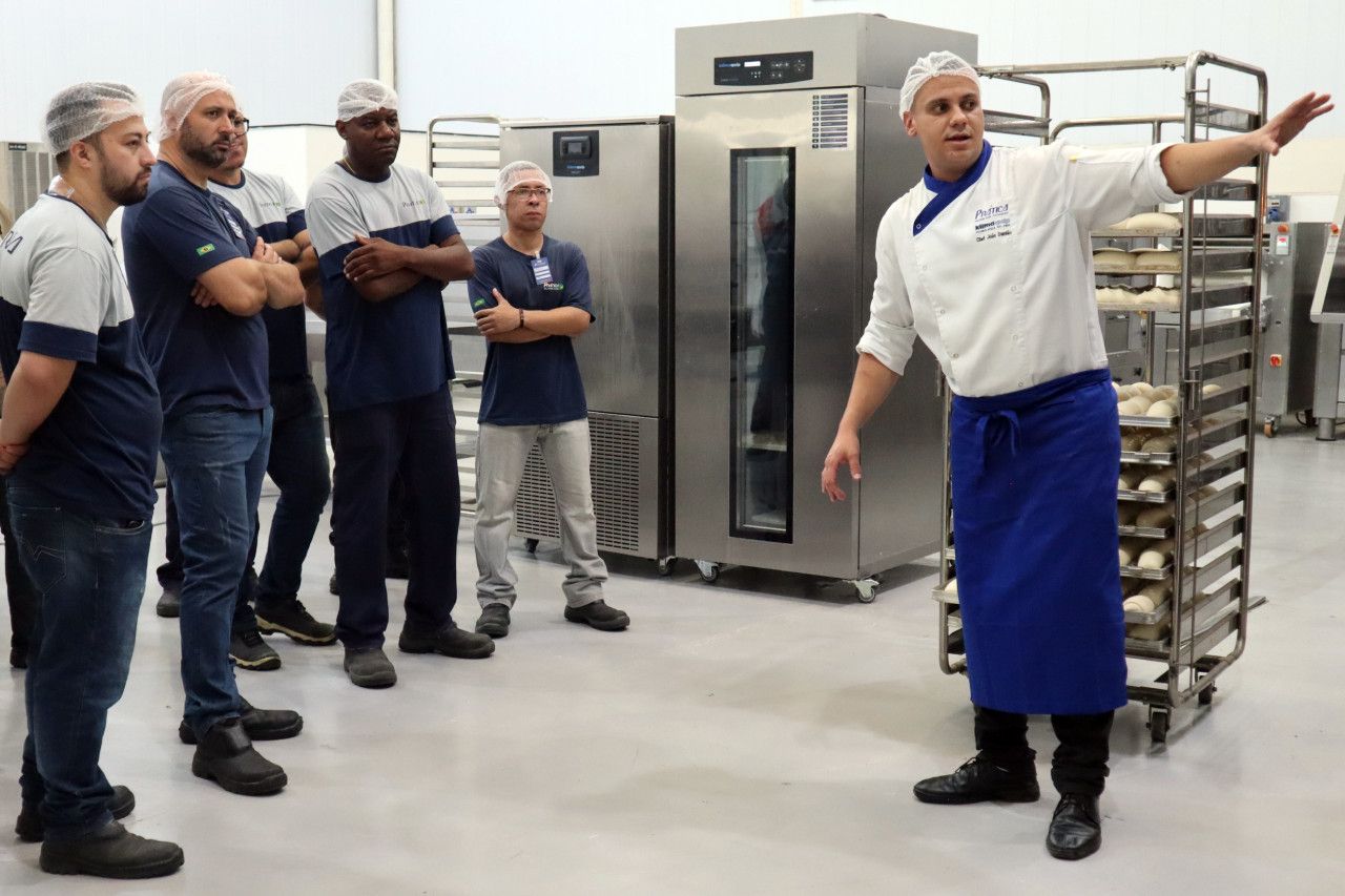 Um homem de avental azul está conversando com um grupo de homens em uma cozinha.