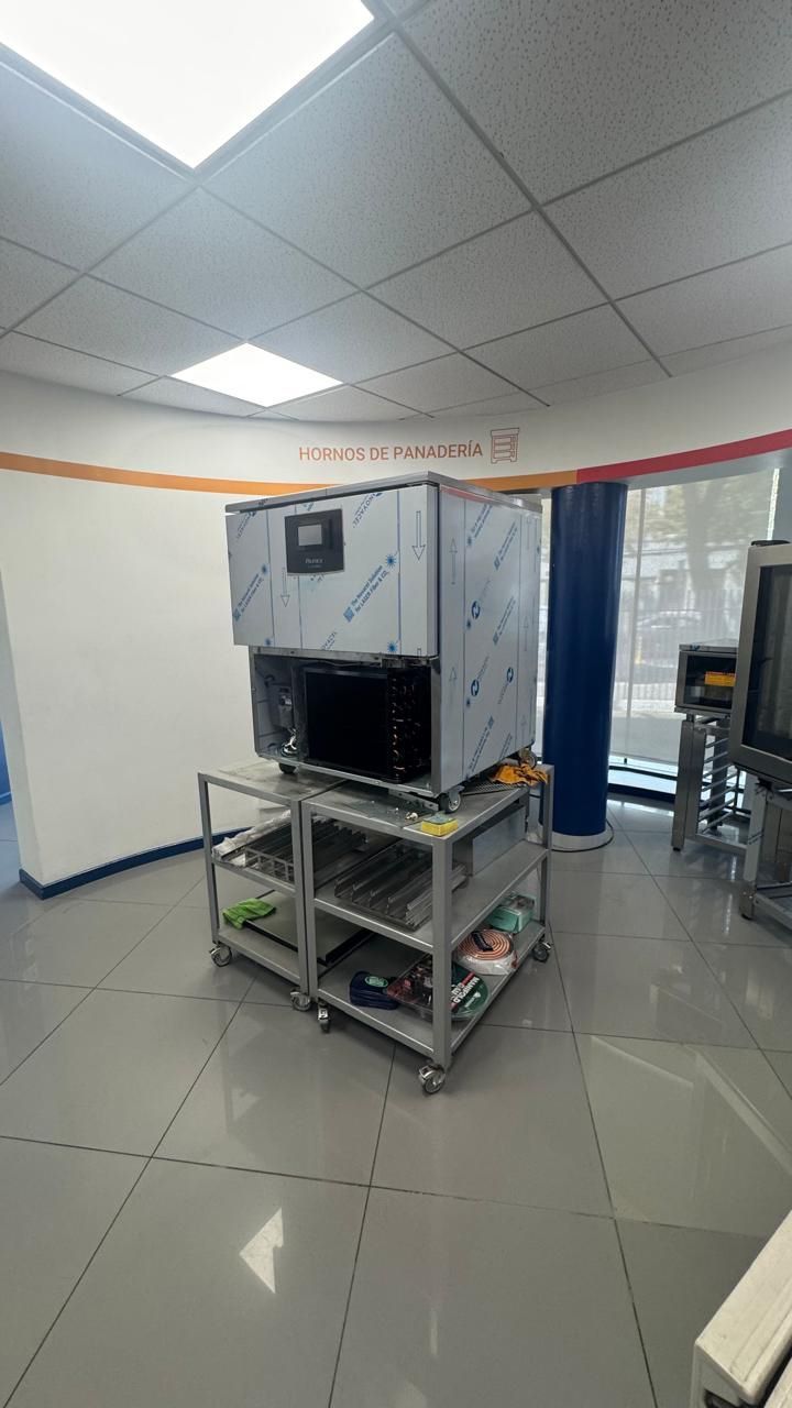 Máquina de gelo sobre um carrinho com rodinhas em uma sala com piso de azulejo, possivelmente um laboratório ou escritório.