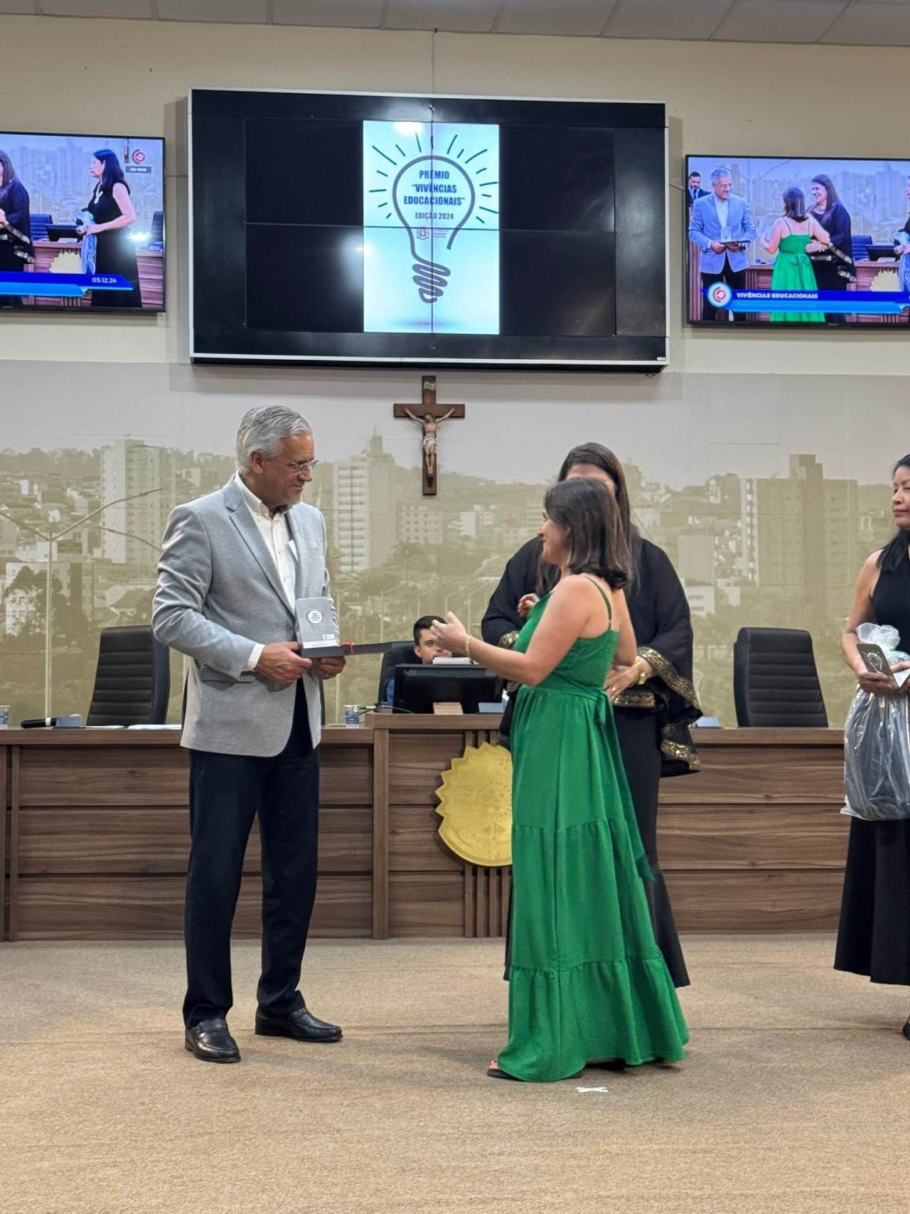 Uma mulher de vestido verde está parada ao lado de um homem de terno em uma sala.