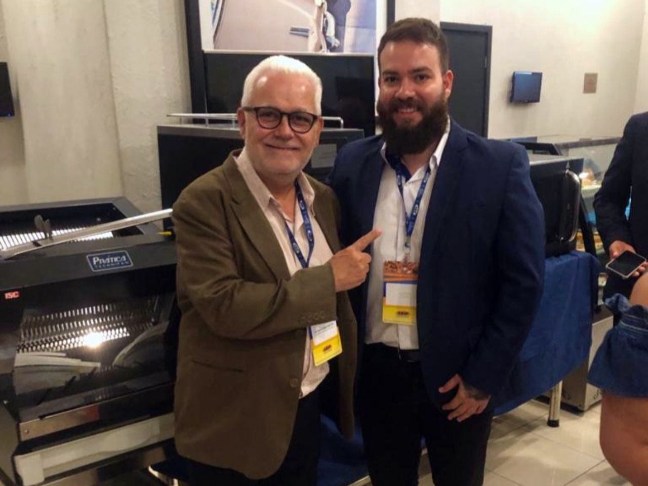 Dois homens estão posando para uma foto em frente a uma máquina.