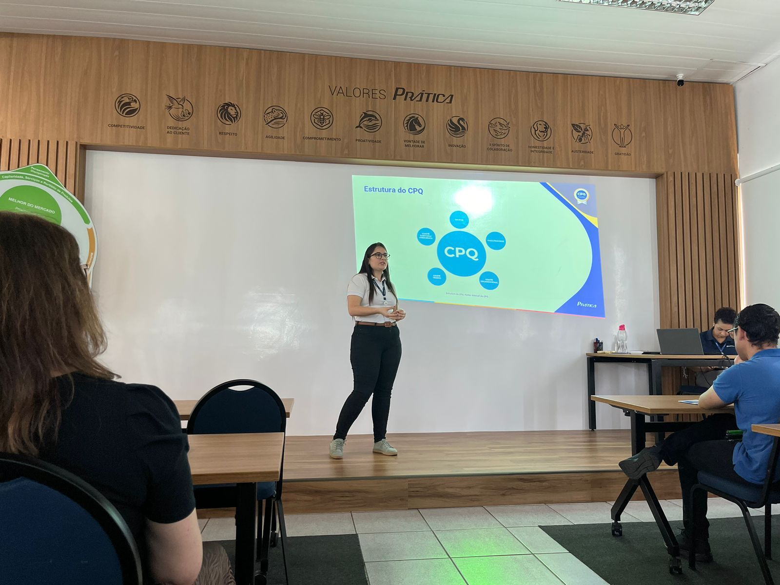 Uma mulher está em um palco fazendo uma apresentação para um grupo de pessoas.