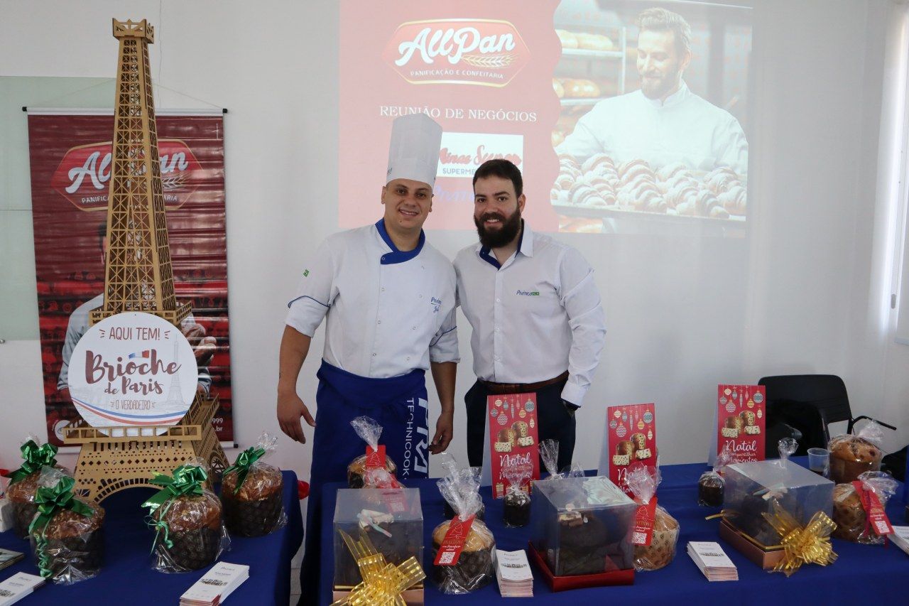 Dois homens estão de pé, um ao lado do outro, em frente a uma mesa cheia de comida.