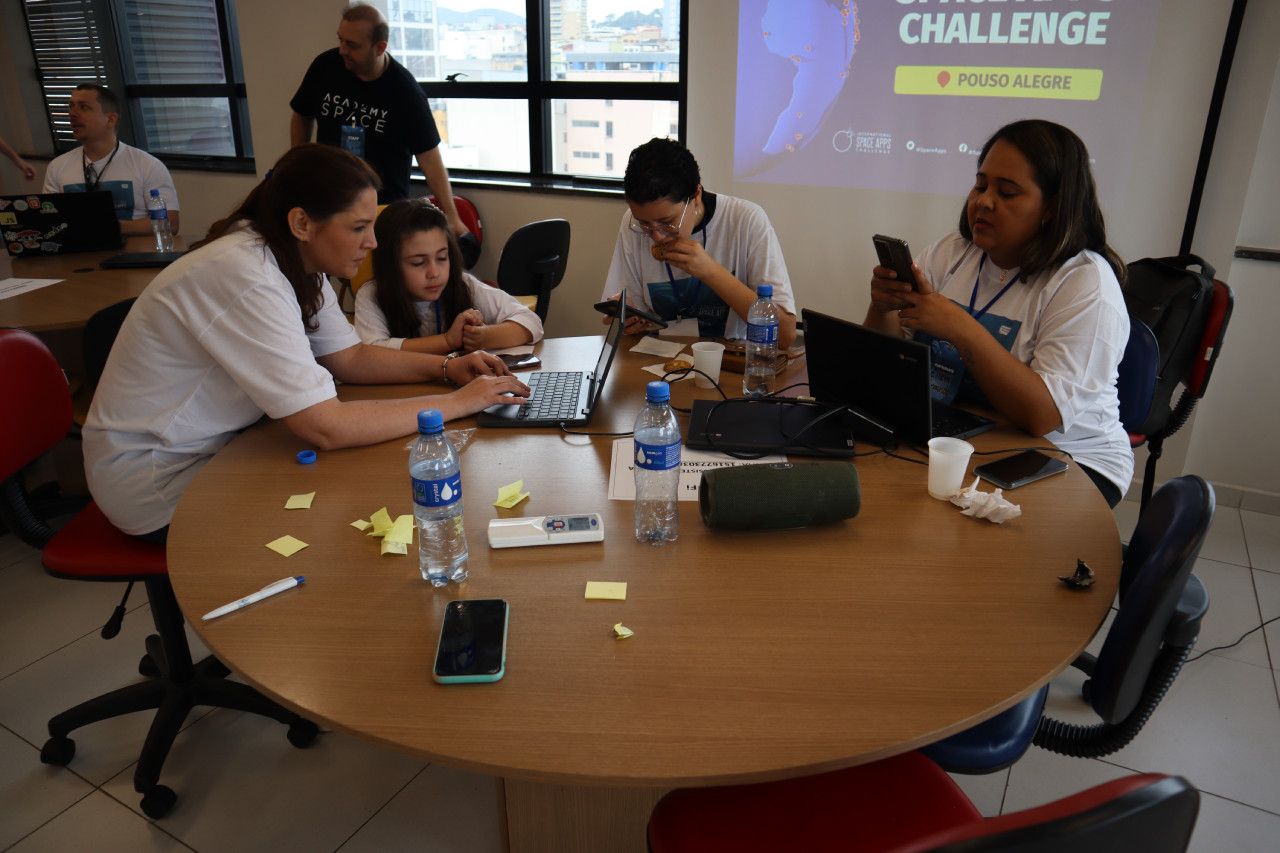 Um grupo de pessoas está sentado ao redor de uma mesa com laptops.