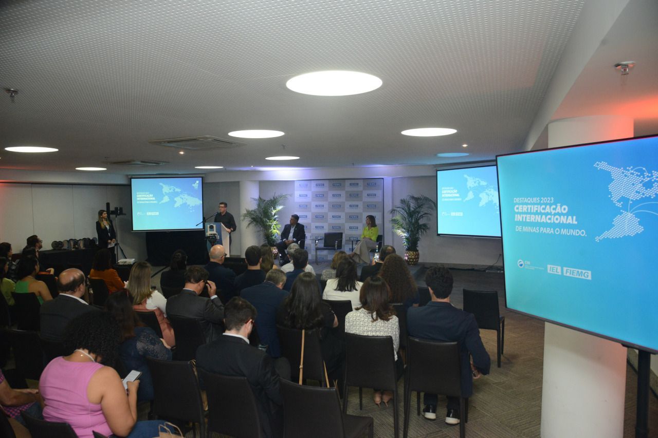 Um grupo de pessoas está sentado em frente a uma tela grande em uma sala.