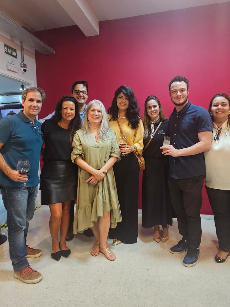 Um grupo de pessoas está posando para uma foto em frente a uma parede vermelha.