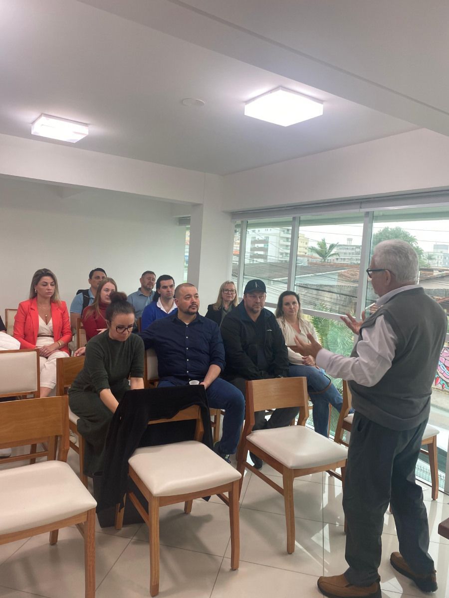 Um homem está de pé na frente de um grupo de pessoas sentadas em cadeiras.