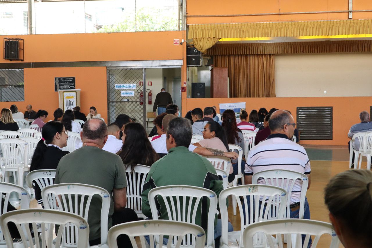 Um grupo de pessoas está sentado em cadeiras de plástico em uma sala.