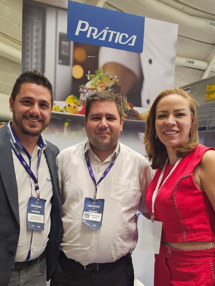 Três pessoas posando para uma foto em frente a uma placa que diz prática