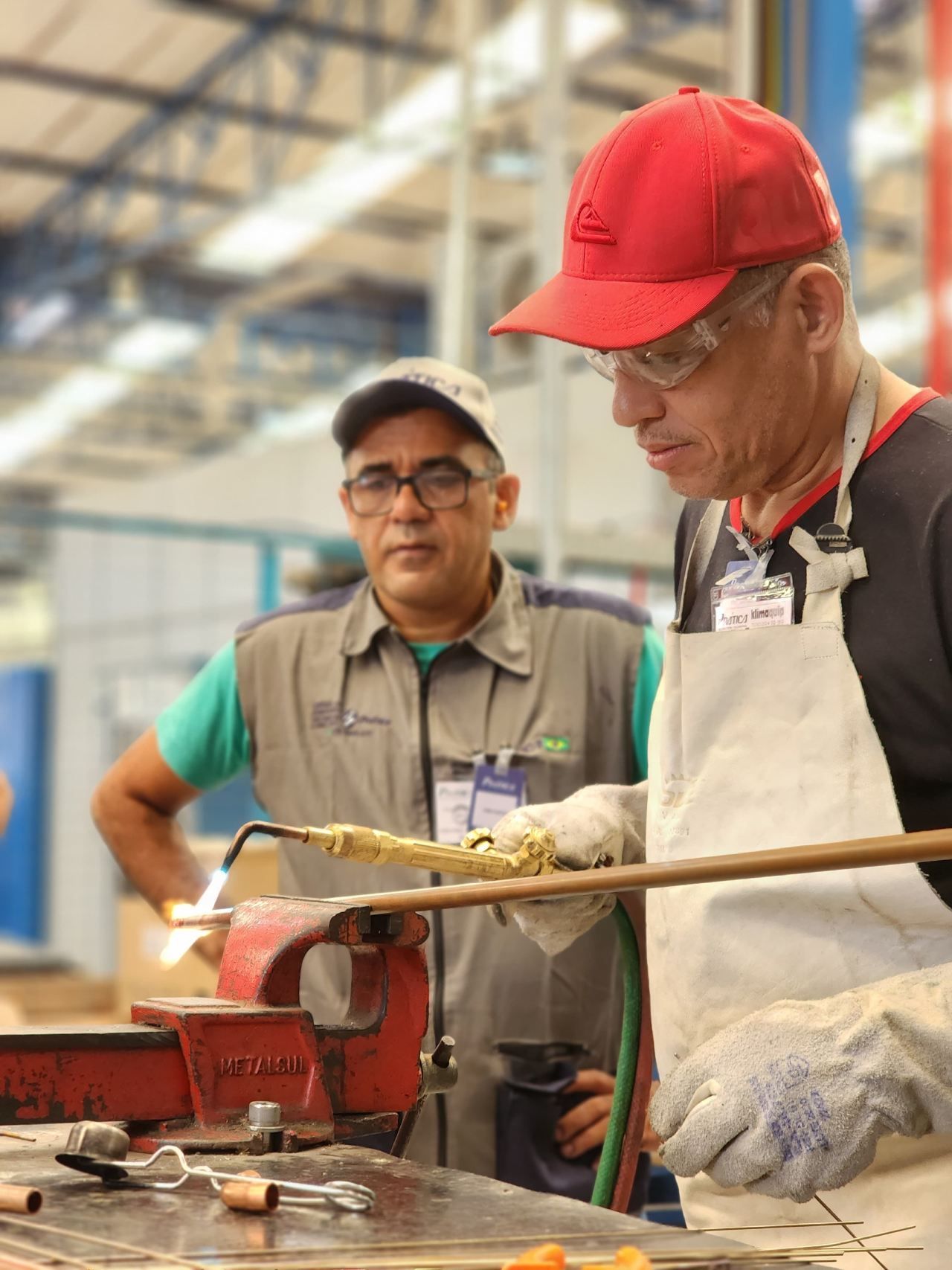 Dois homens estão trabalhando em uma peça de metal em uma fábrica.