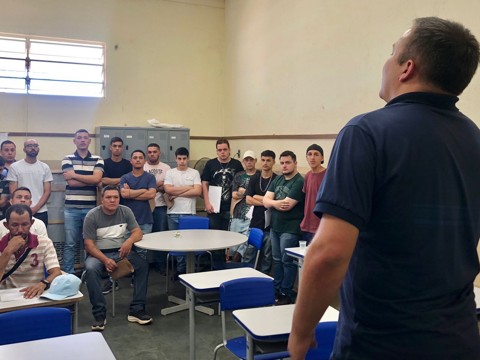 Um homem está parado na frente de um grupo de homens em uma sala de aula.