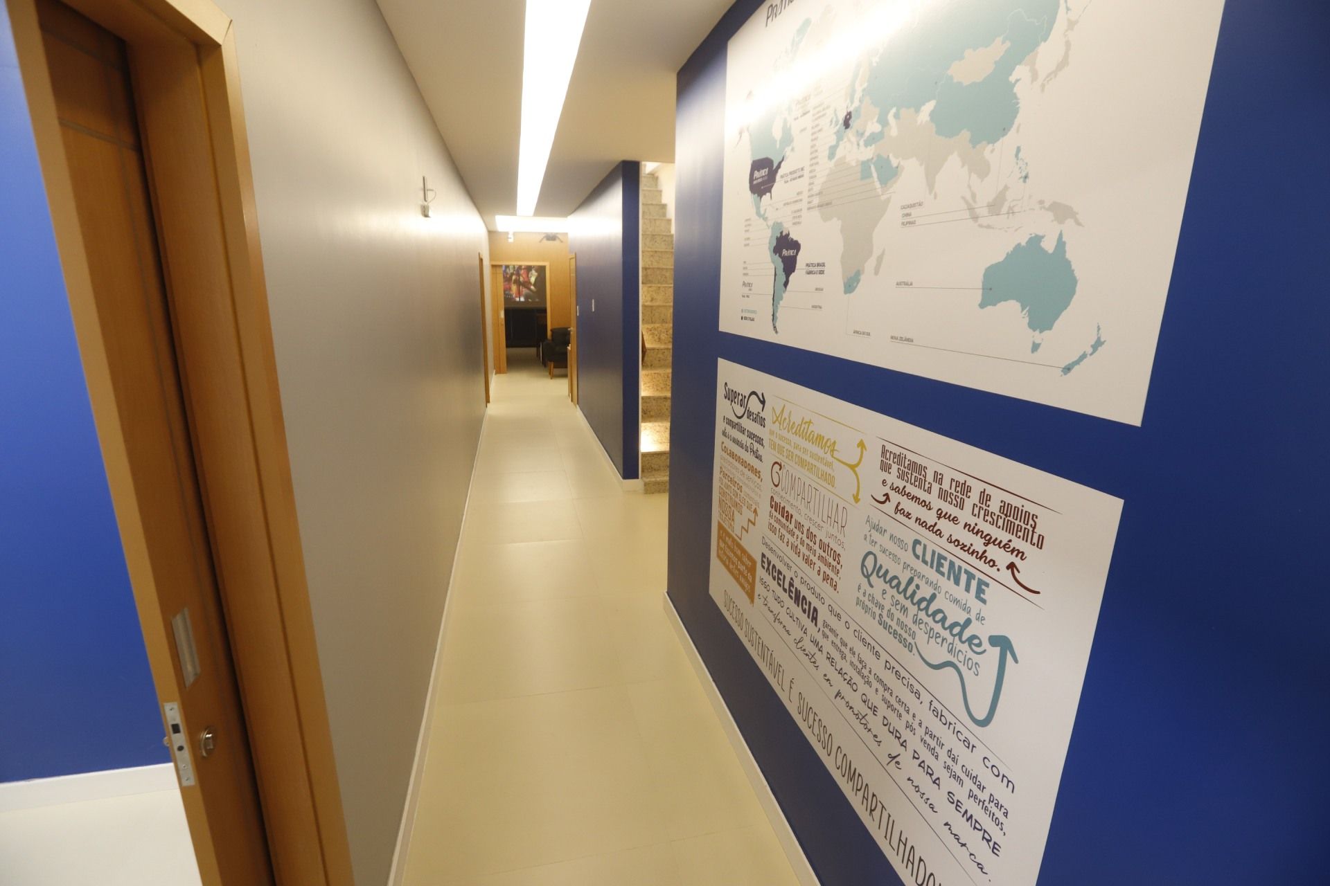 Corredor estreito com paredes azuis e cinzas, um mapa e um pôster. Uma porta à esquerda.